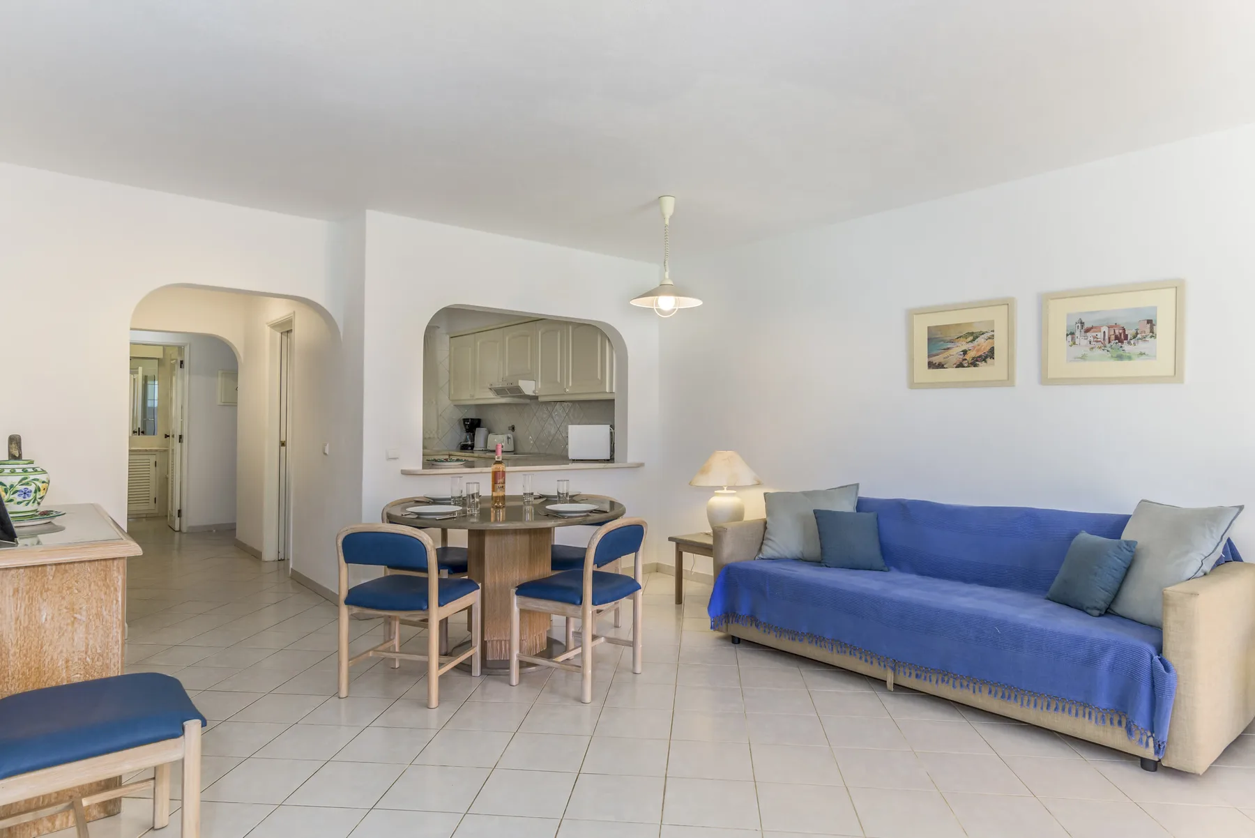 A living and dining area with blue seating beside a small kitchen.
