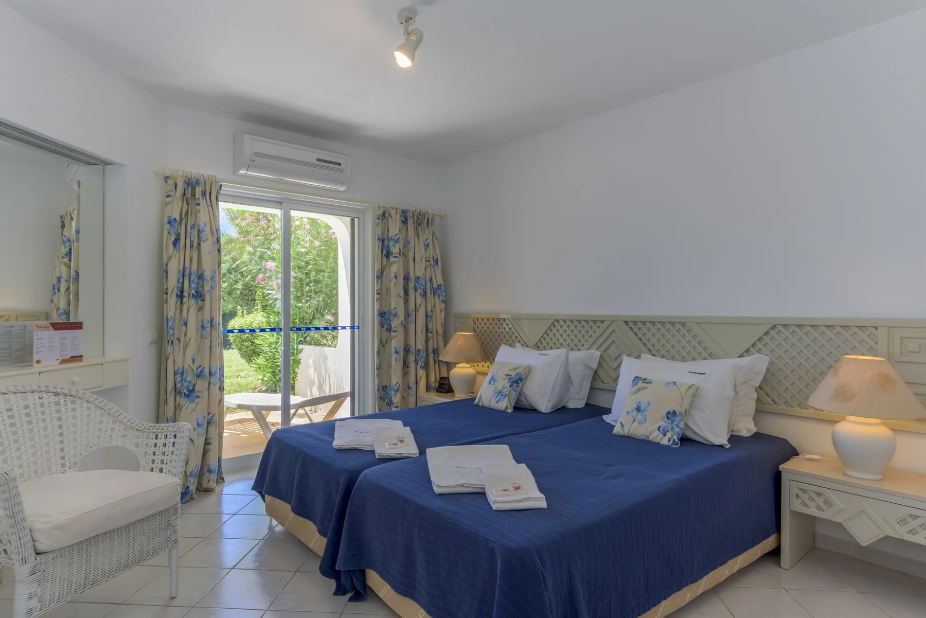 Un dormitorio con dos camas vestidas de azul y una puerta de cristal que da a un jardín.