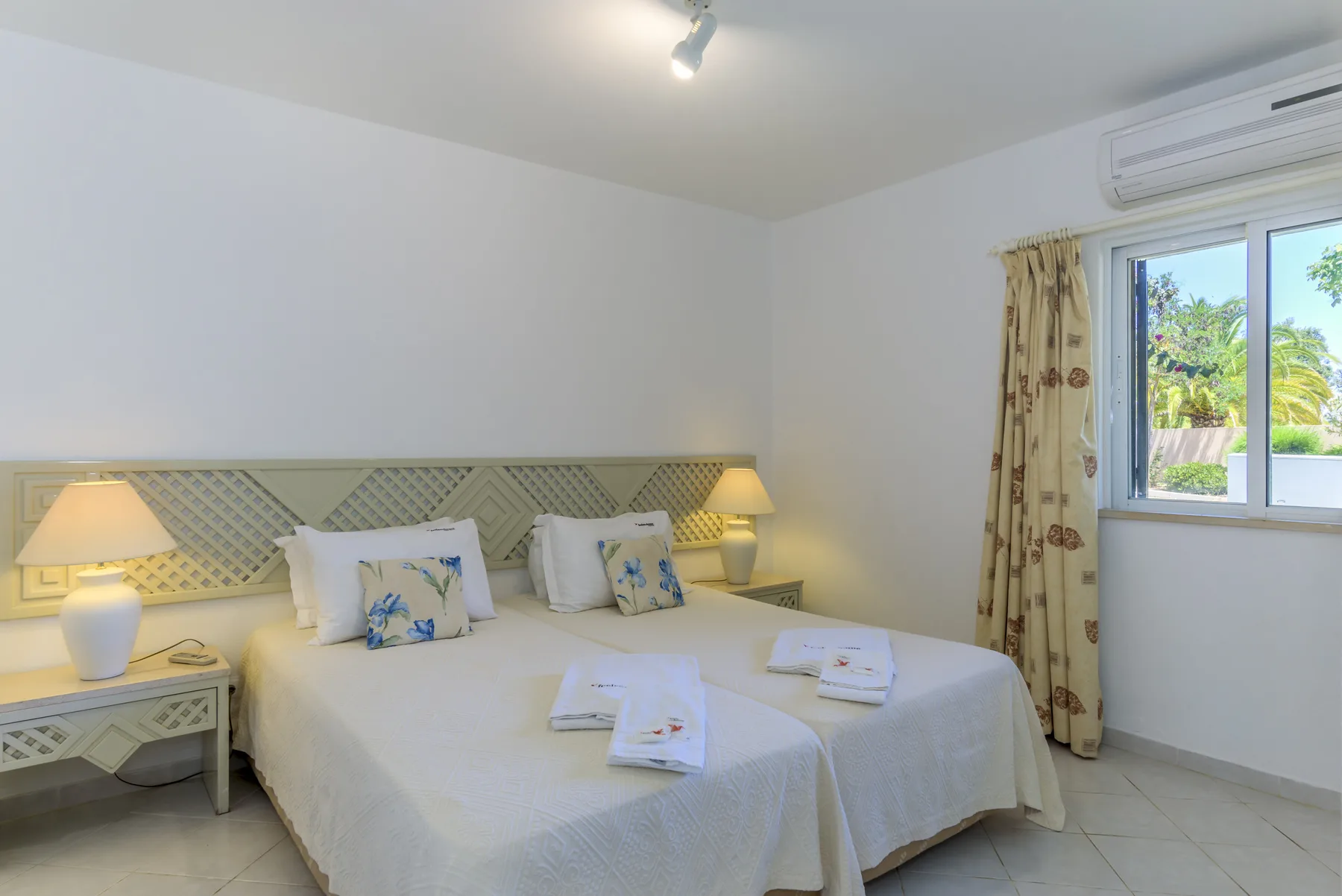 Un dormitorio luminoso con una cama doble, mesillas y una ventana con vistas a la vegetación.