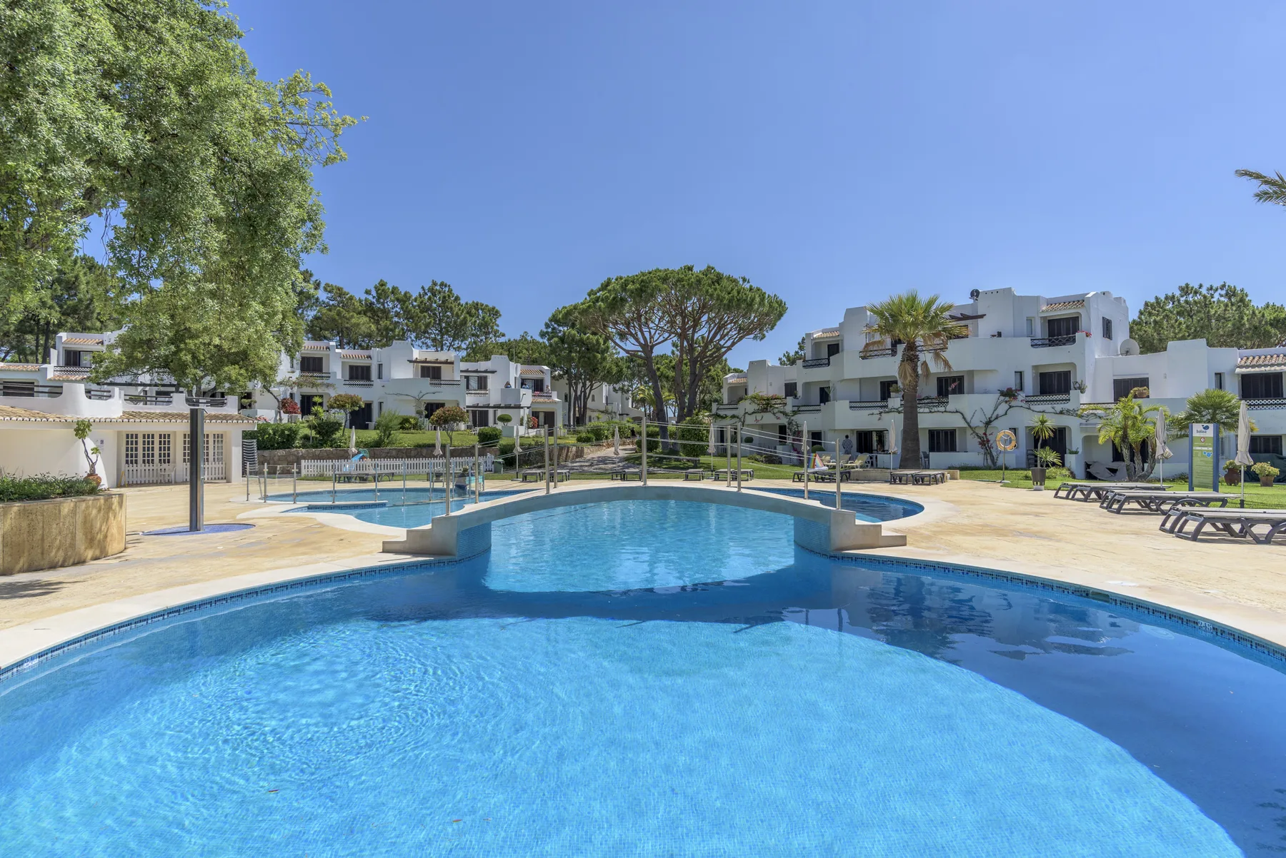 An outdoor swimming pool sits among low-rise buildings and trees.