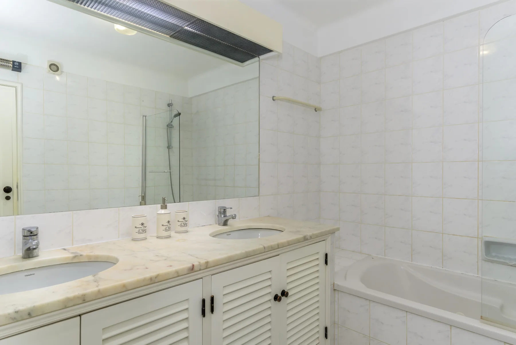 Un baño luminoso con un lavabo largo, espejo de pared y bañera.