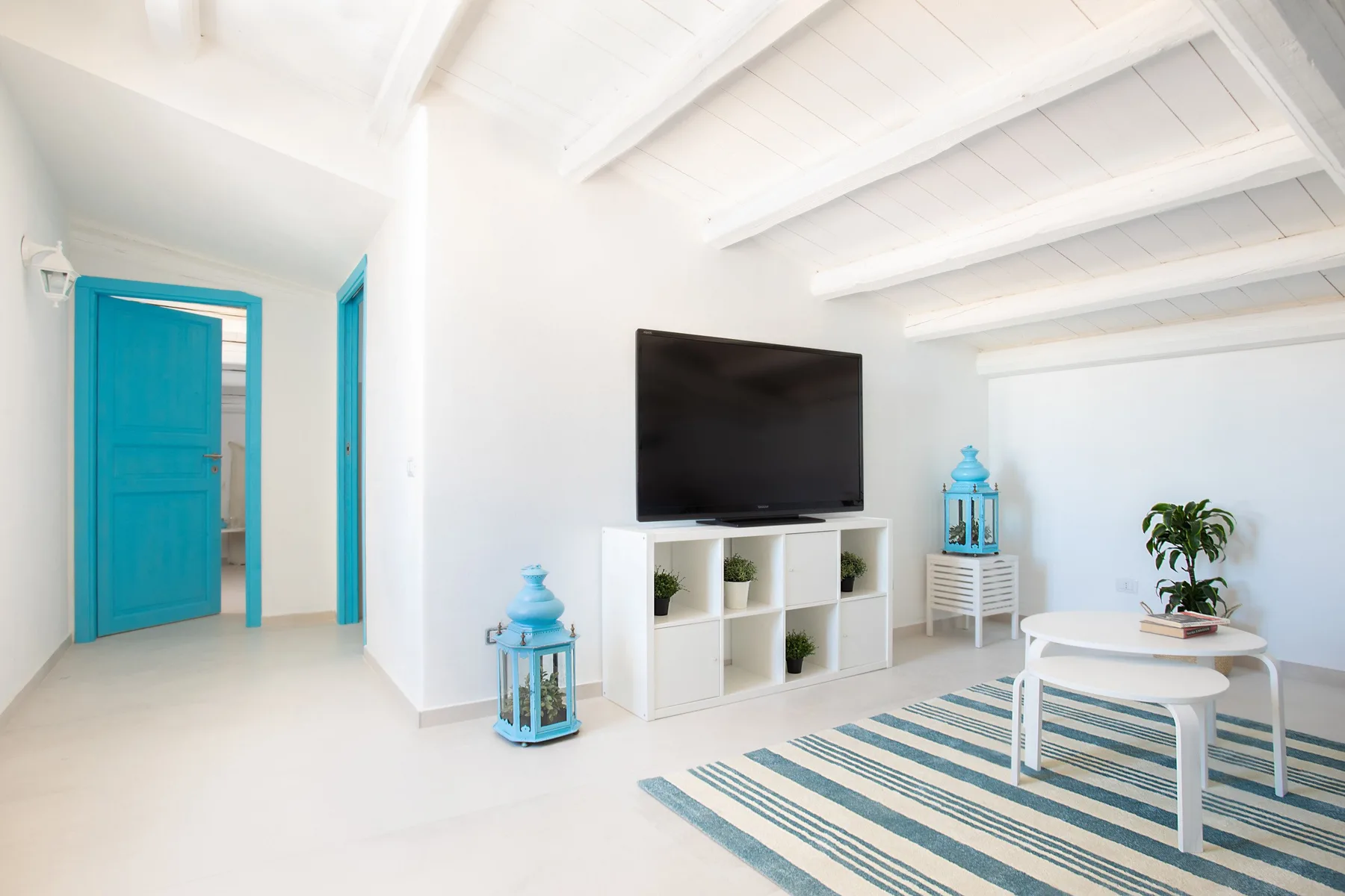 A bright living room with a television, white shelving, and a striped rug.