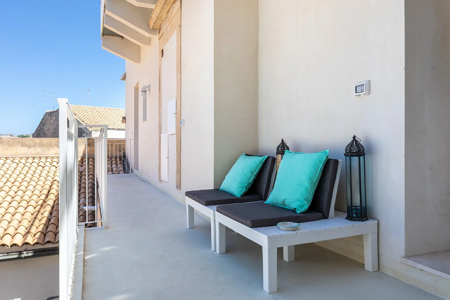 A balcony with two lounge seats and turquoise cushions beside a light-colored wall.