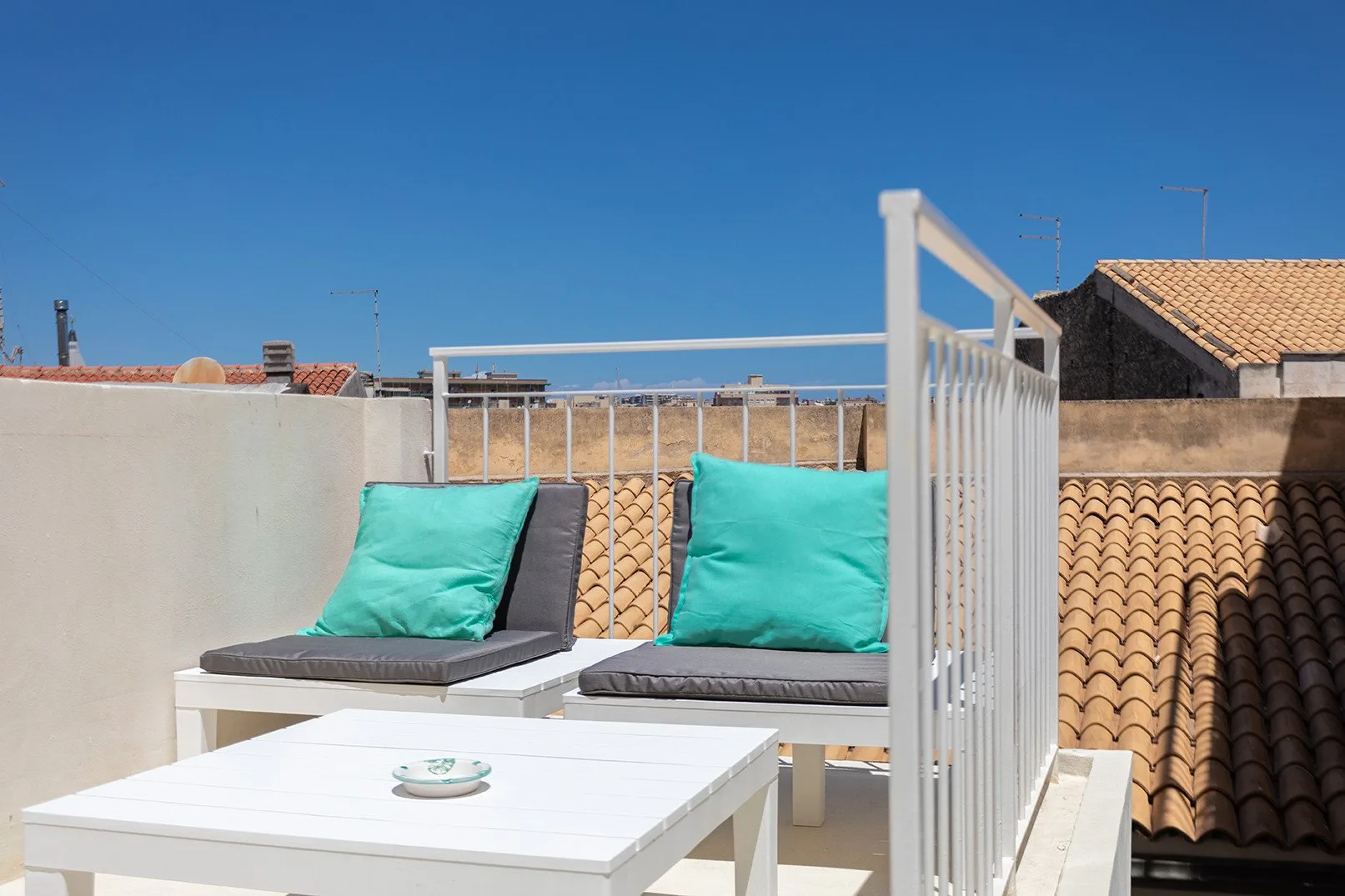 A rooftop terrace seating area with turquoise cushions and a white table.
