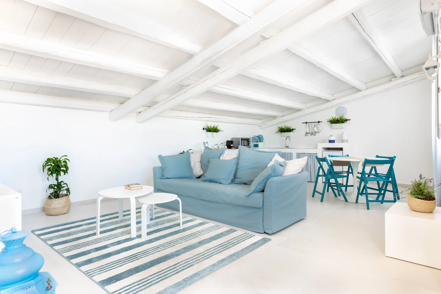A bright living area with blue seating, a striped rug, and a dining table.
