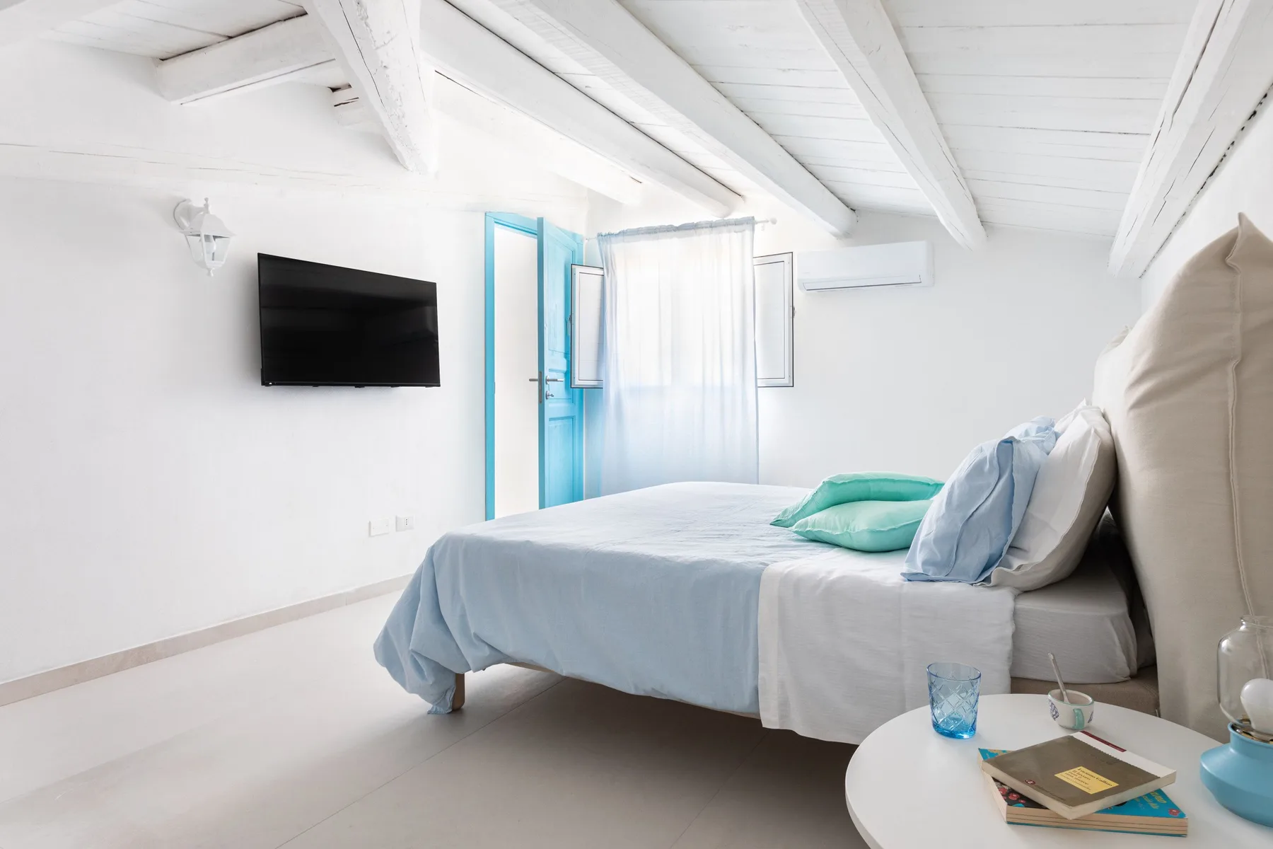 A bright bedroom with a bed, blue bedding, and a wall-mounted television.