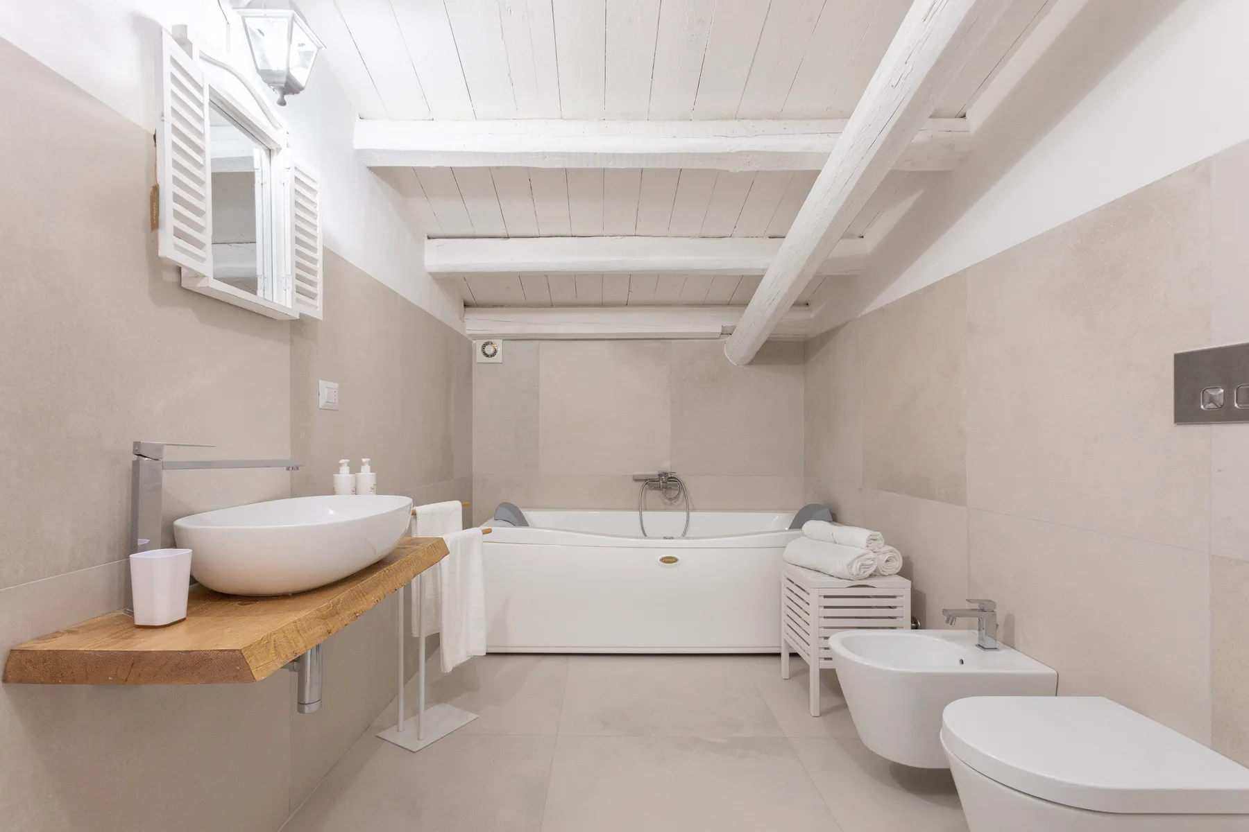 A bright bathroom with a bathtub, vessel sink, and white ceiling beams.