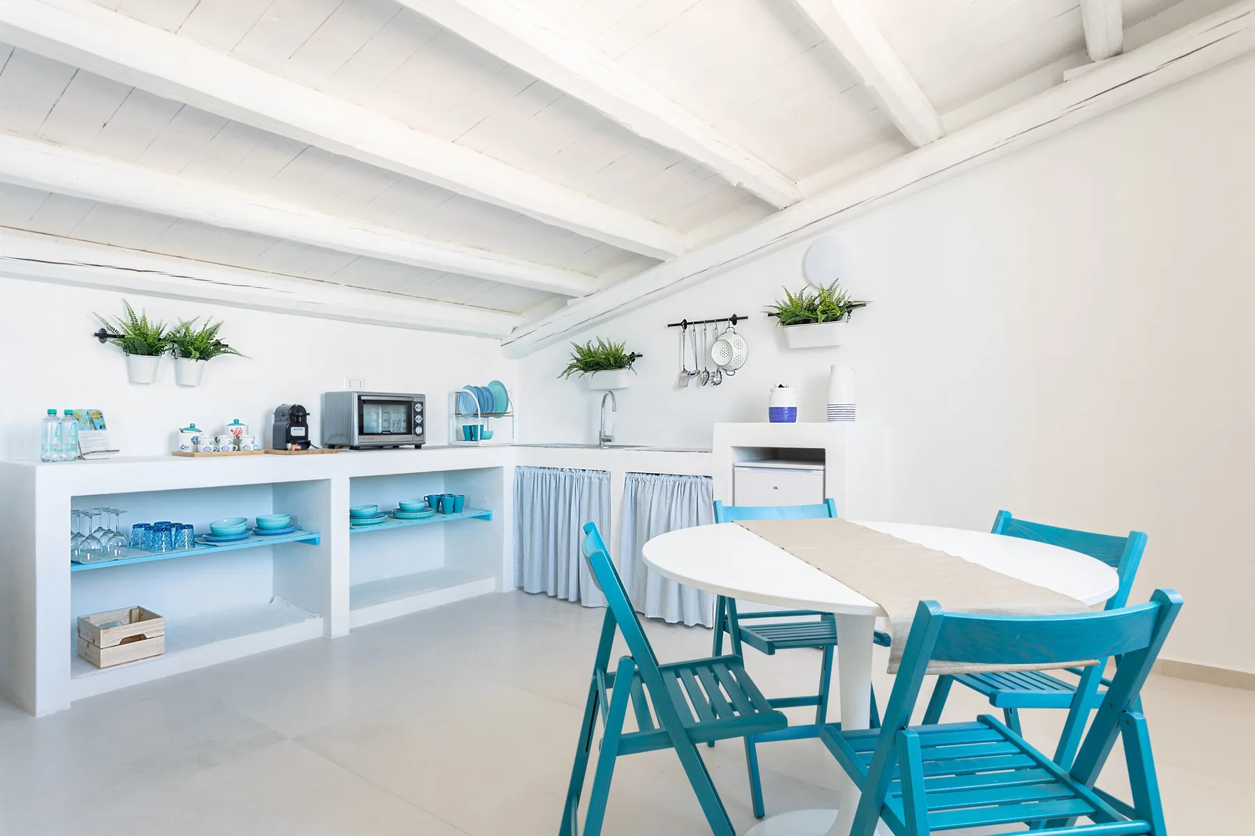 A bright dining and kitchen area with a table, turquoise seating, and open shelves.