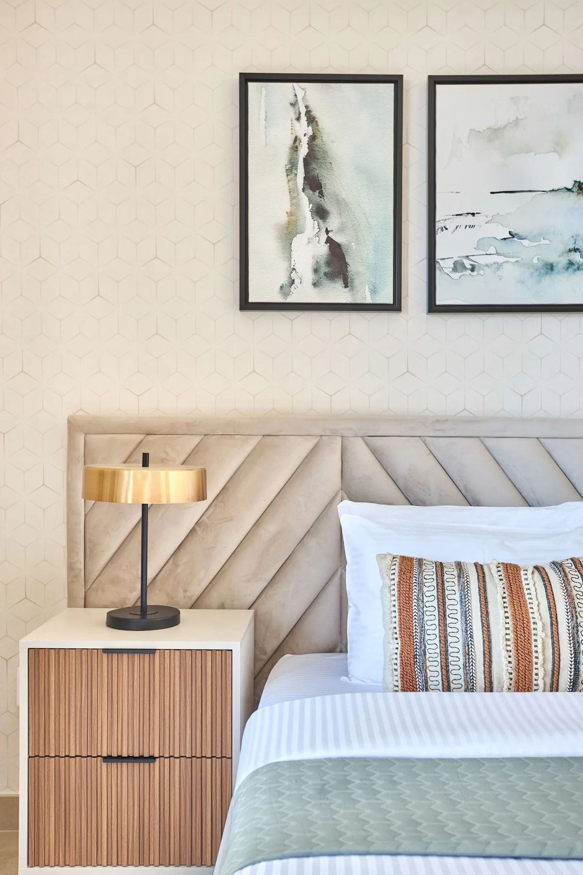 Un dormitorio con una cama junto a una mesita de madera y cuadros enmarcados.