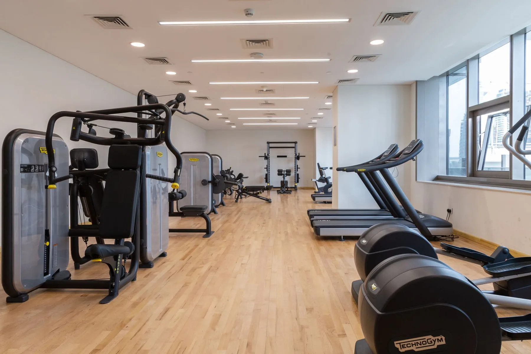 Un gimnasio con máquinas de ejercicio y cintas de correr sobre un suelo de aspecto madera.