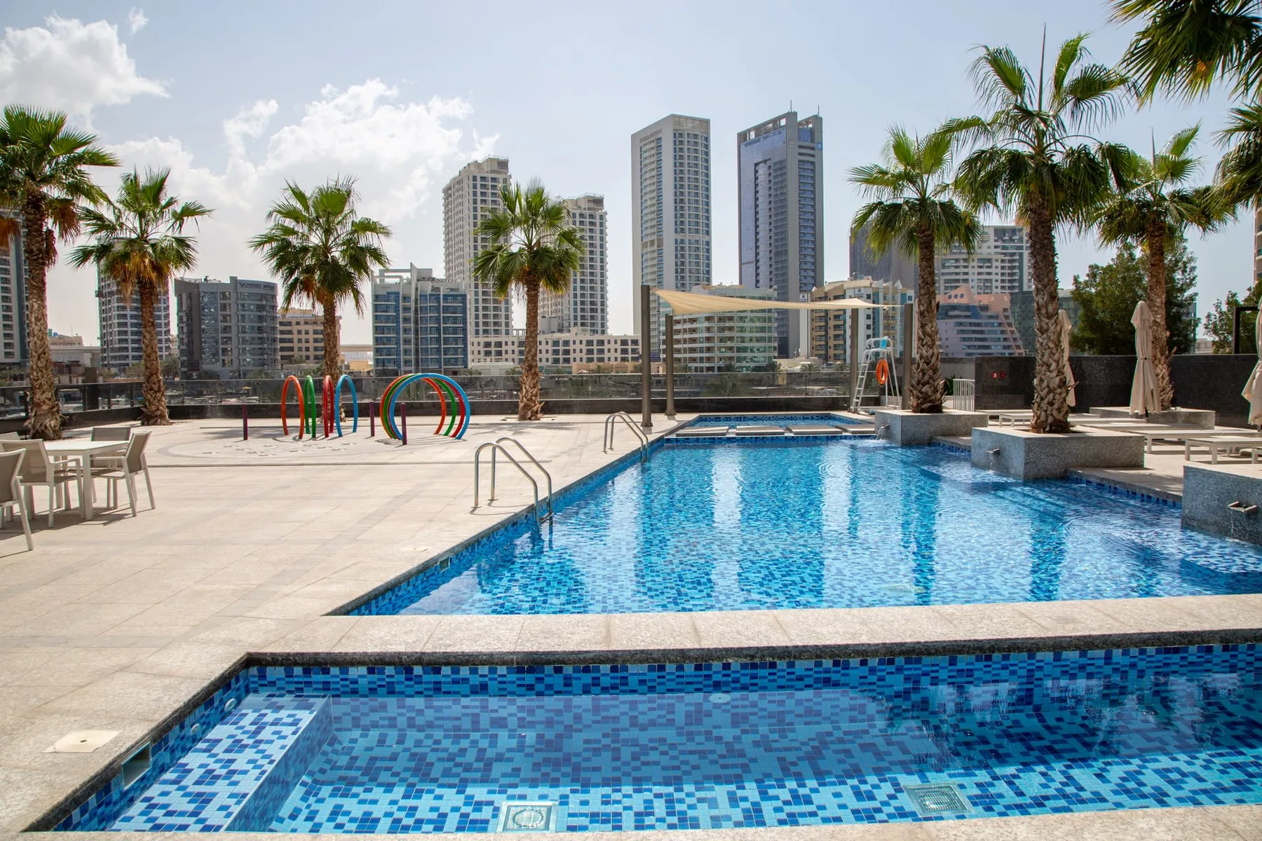 Una piscina al aire libre está junto a otra piscina de azulejos y palmeras.