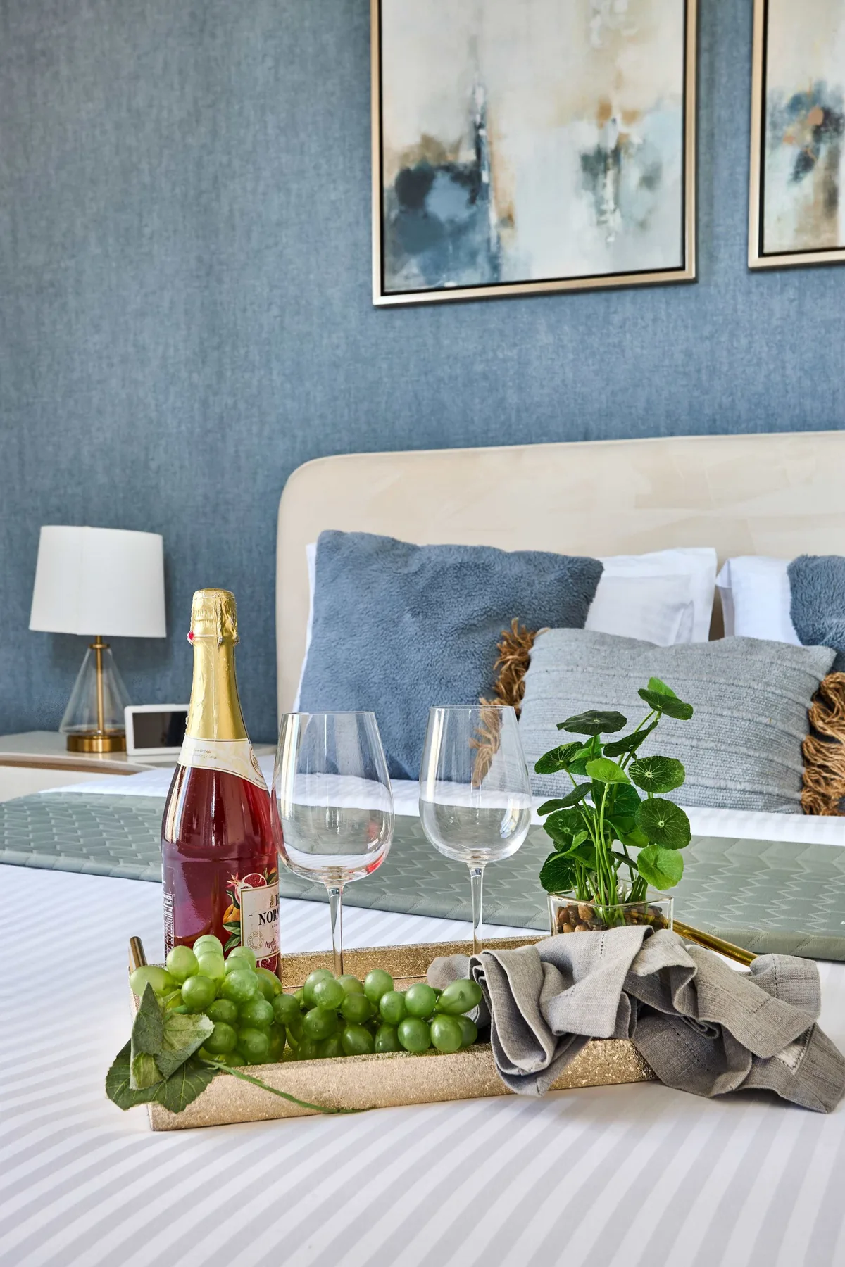 Un dormitorio con una cama, cuadros enmarcados y una bandeja con fruta y bebidas.