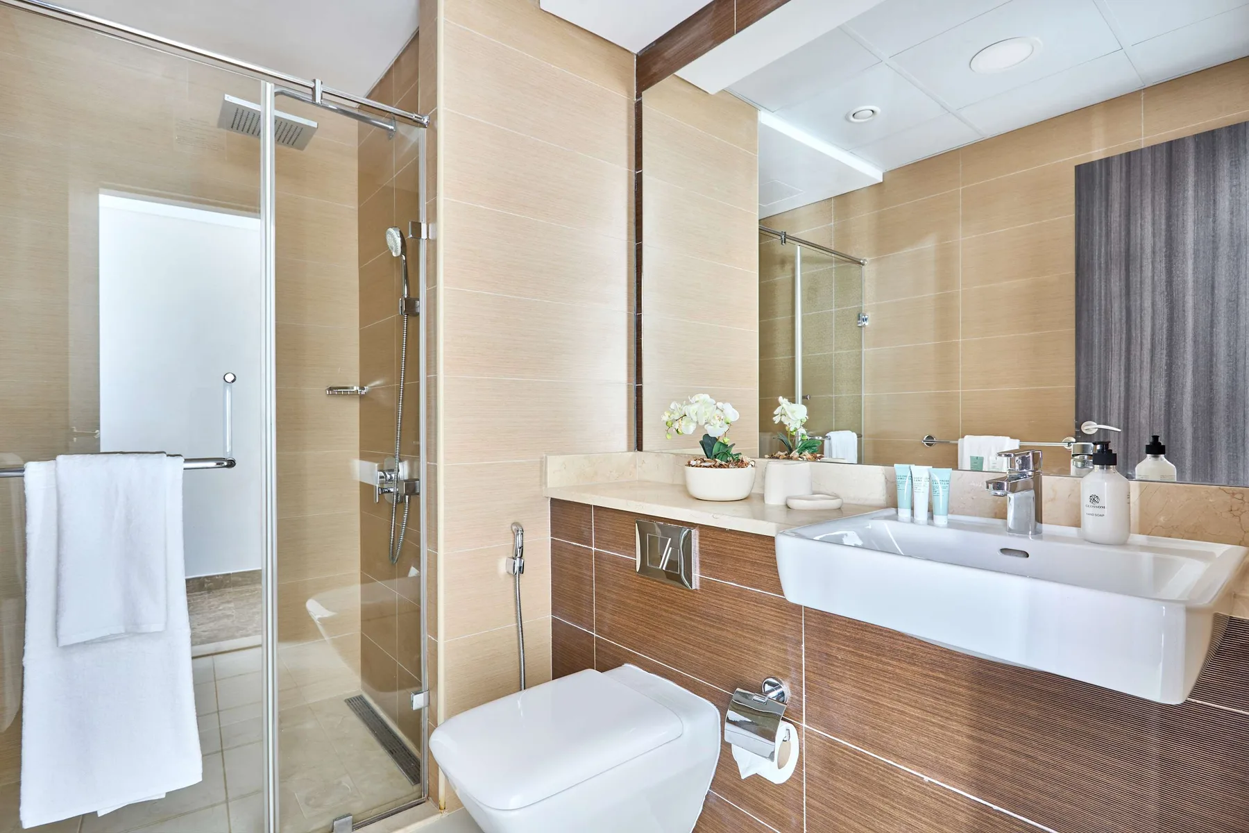 Un baño alicatado con ducha de vidrio, inodoro y una larga encimera con lavabo.