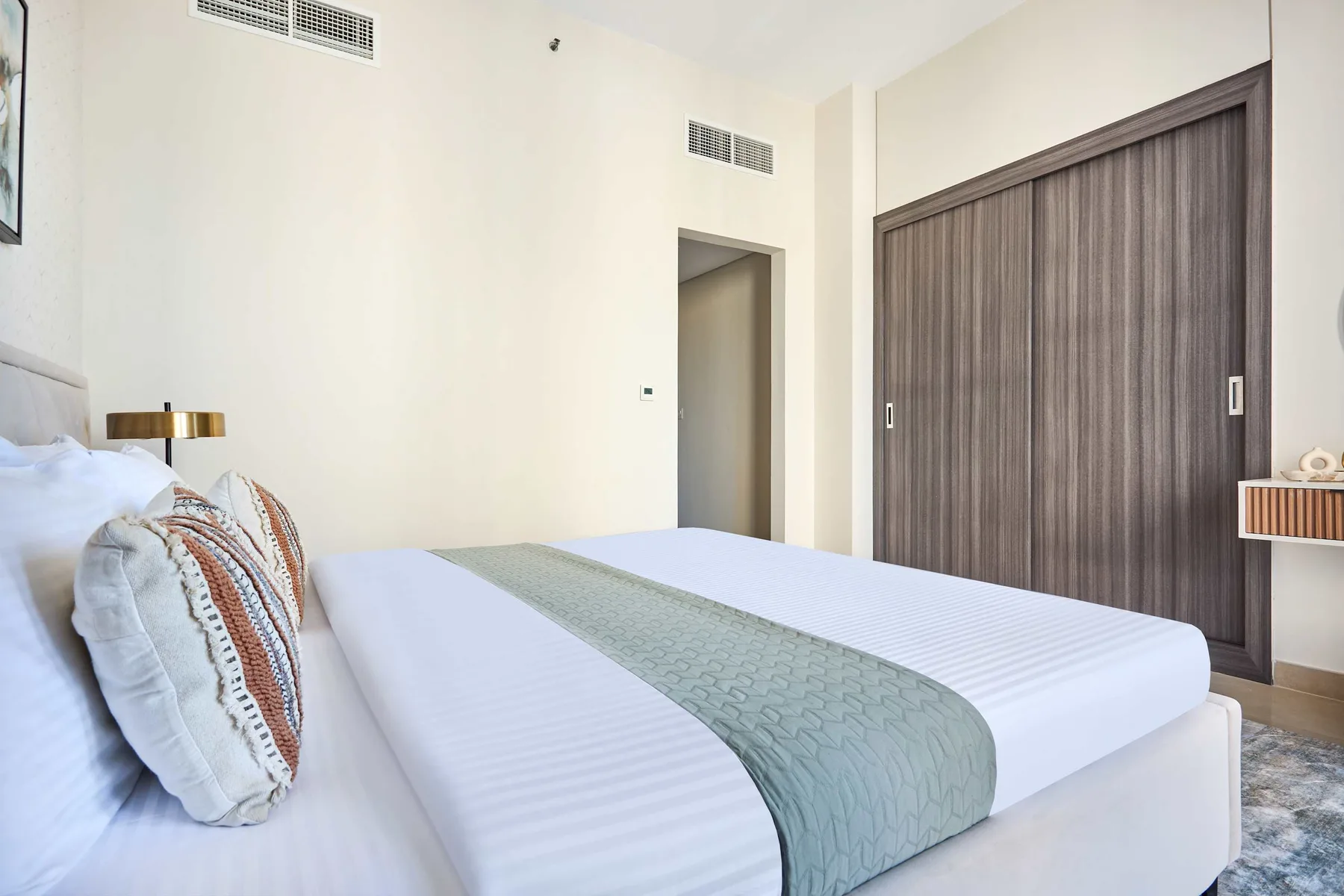 Un dormitorio con una cama bien tendida y un camino verde apagado.