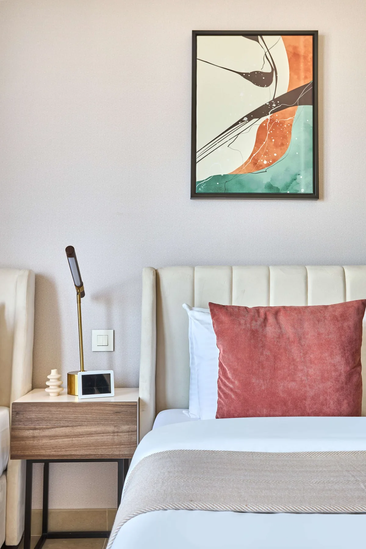 Un dormitorio con una cama bien tendida, una mesita de noche y arte abstracto en la pared.