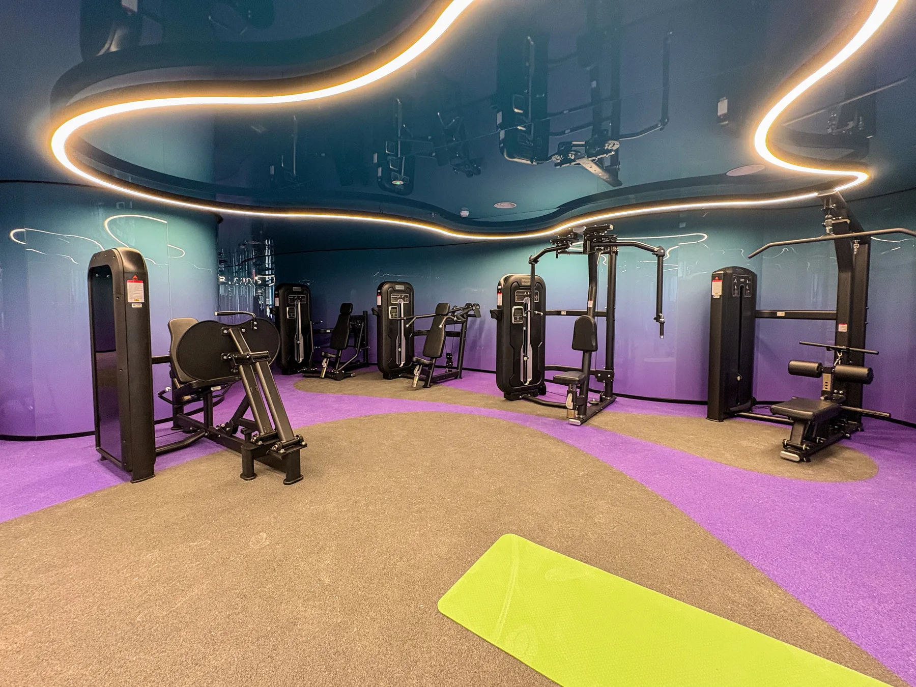 Un gimnasio con máquinas de ejercicio y una esterilla verde brillante en el suelo.