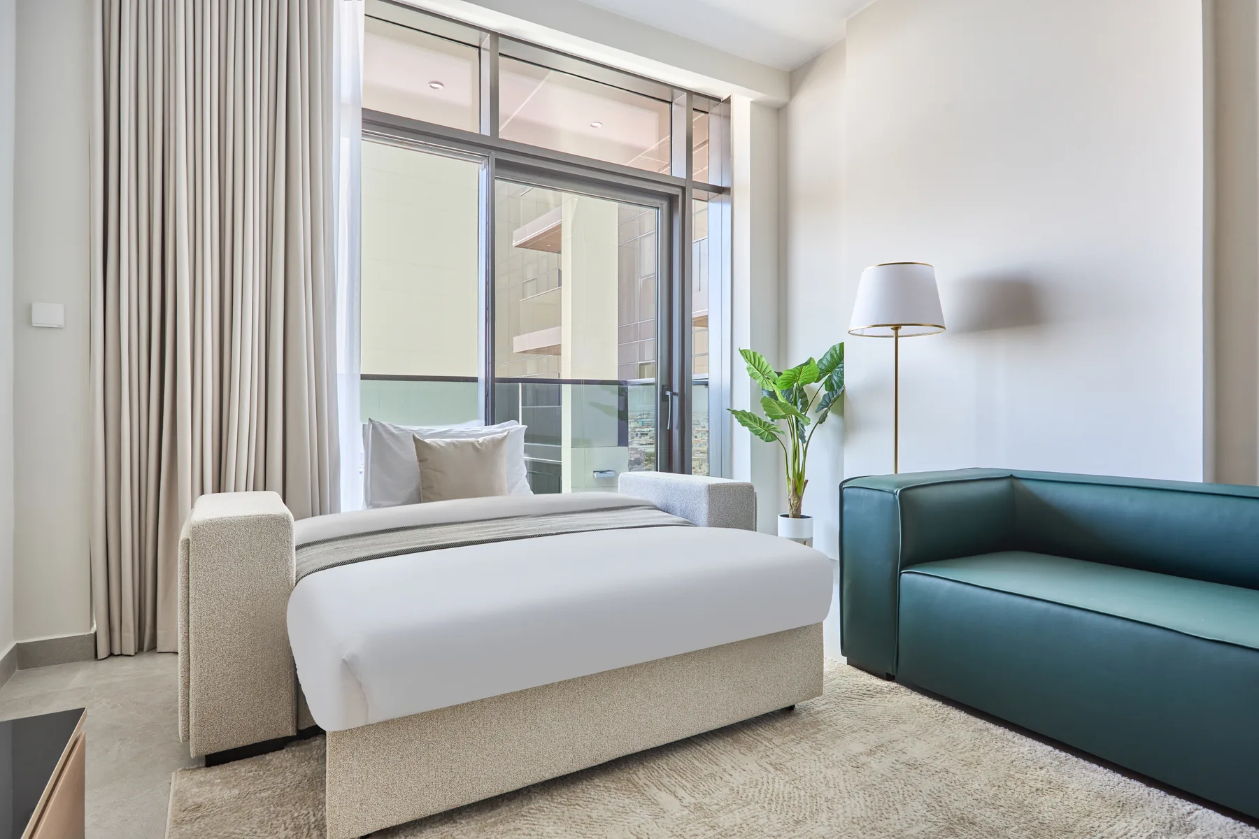 Un dormitorio luminoso con una cama junto a una ventana amplia y un sofá verde azulado.