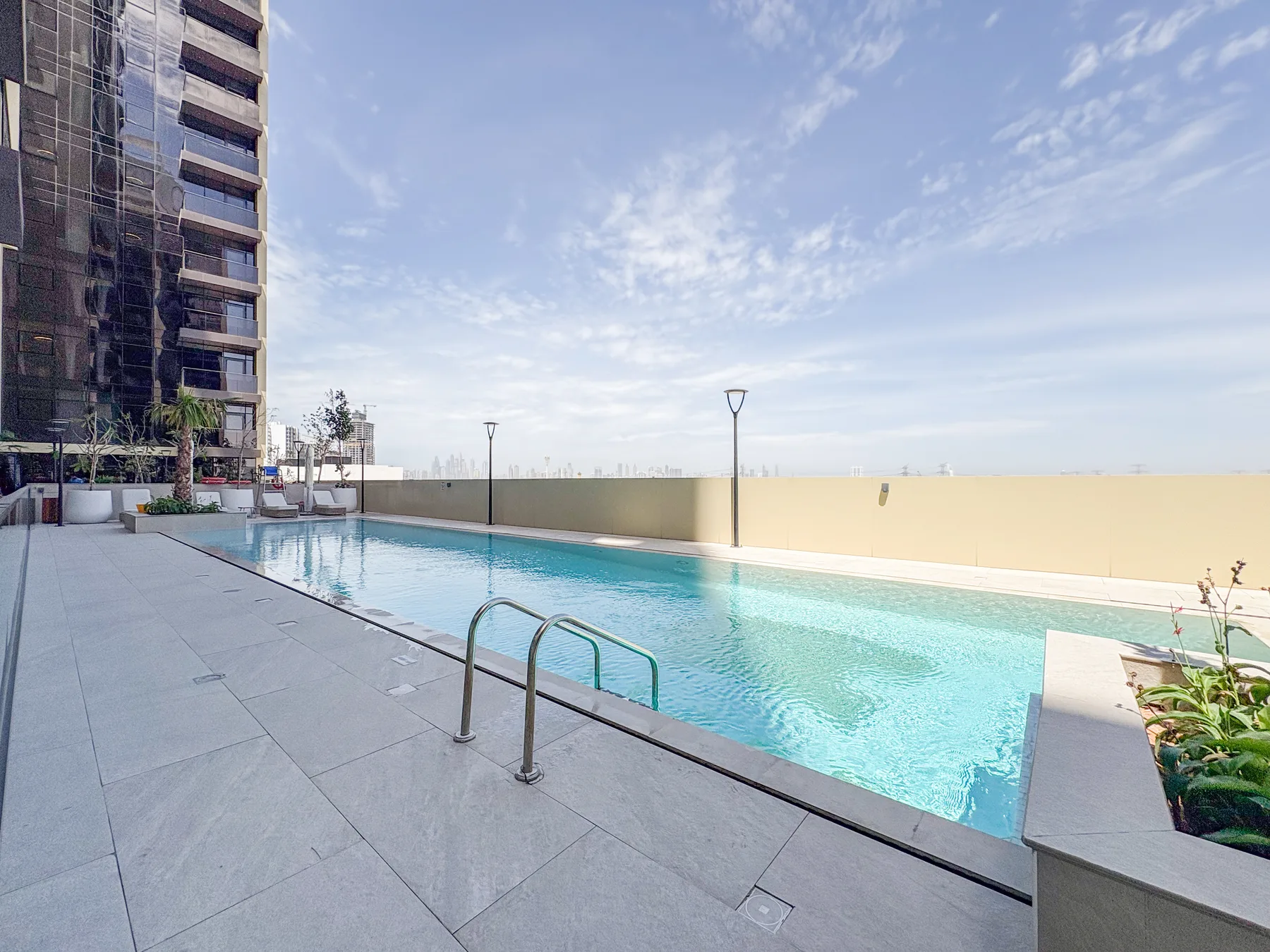 Una piscina al aire libre junto a un edificio alto bajo un cielo despejado.
