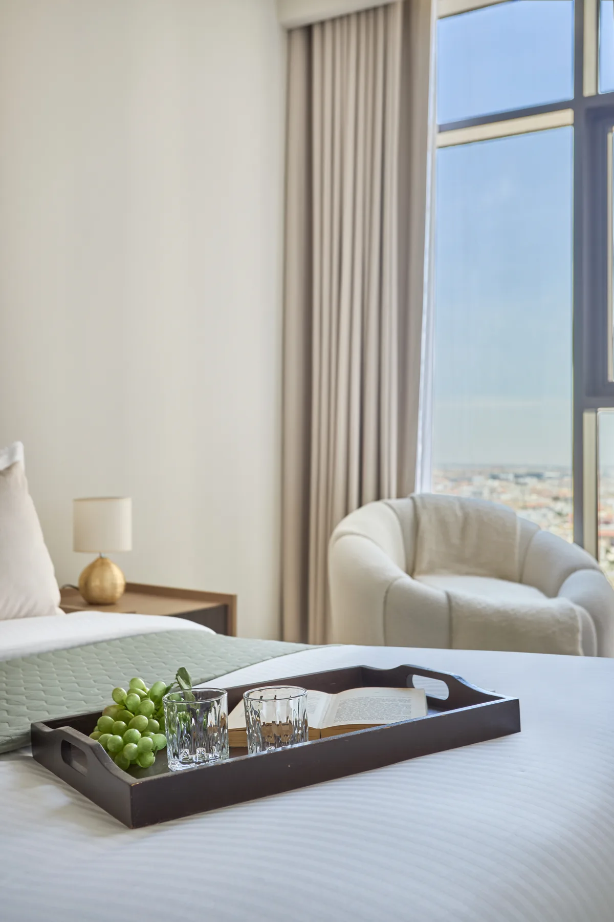 Un dormitorio con una cama bien tendida, un sillón y una ventana grande.
