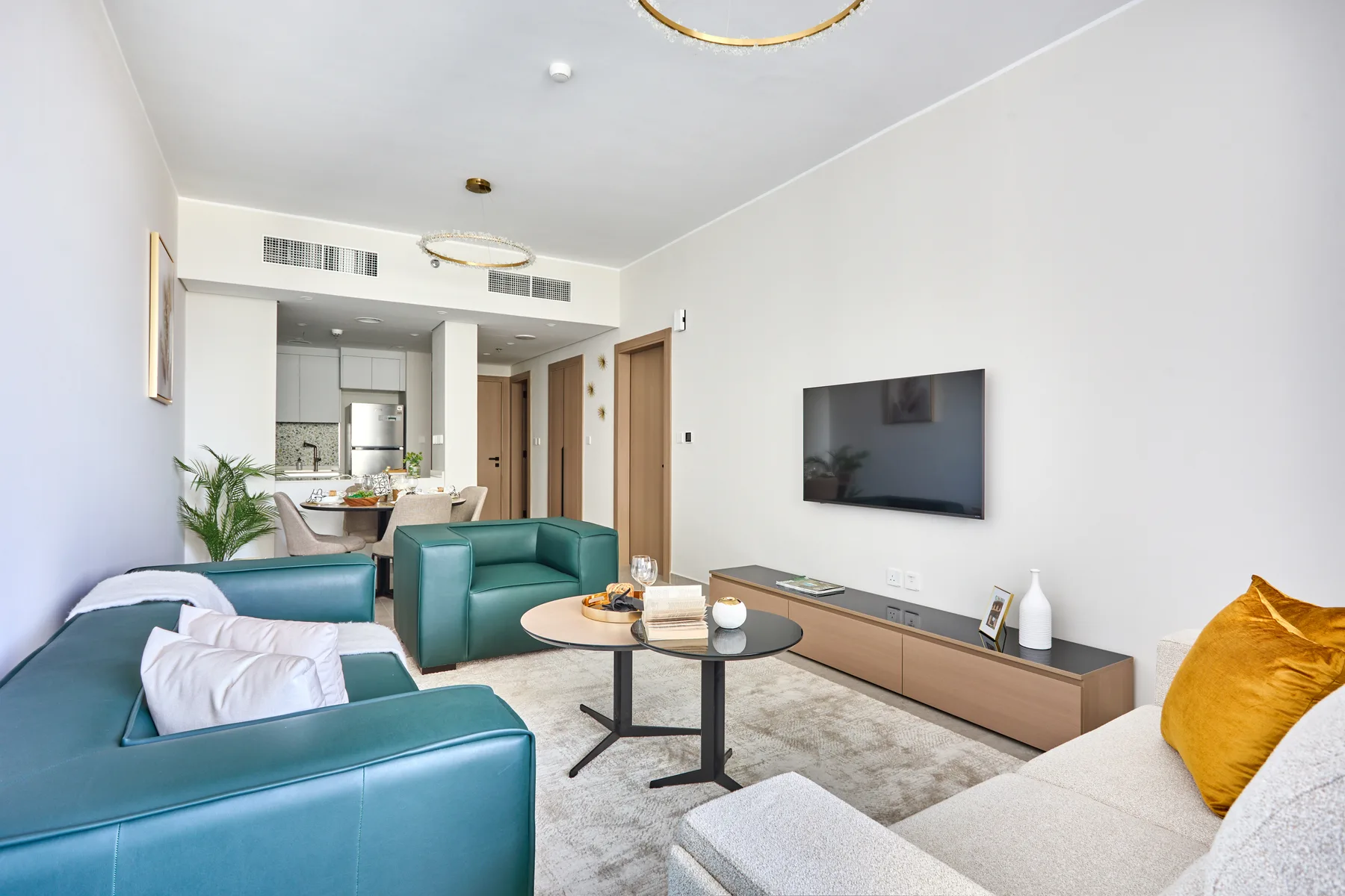 Una sala luminosa con asientos turquesa, un televisor y una mesa de centro redonda.