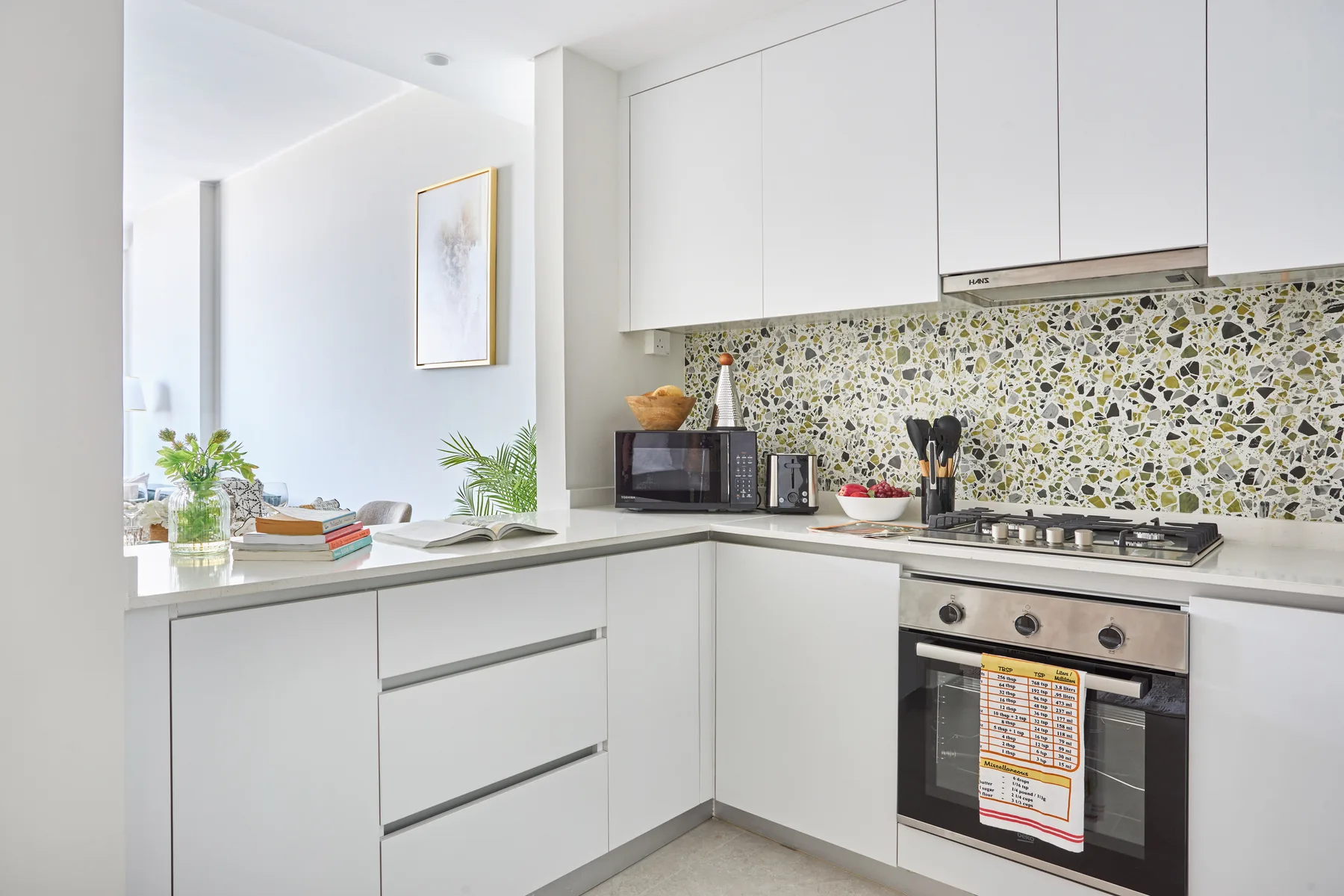 Una cocina luminosa con gabinetes blancos, un salpicadero estampado y un horno sobre la encimera.