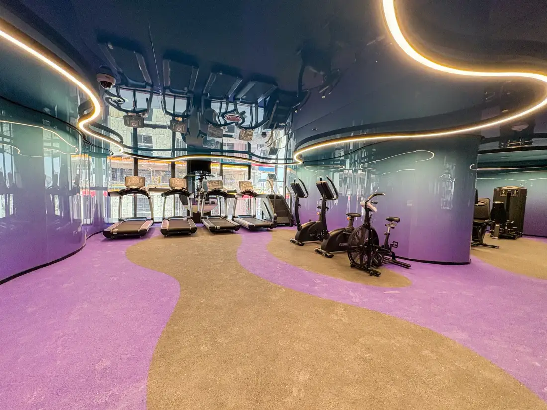 Un gimnasio moderno con máquinas de ejercicio alrededor de un espacio abierto y colorido.