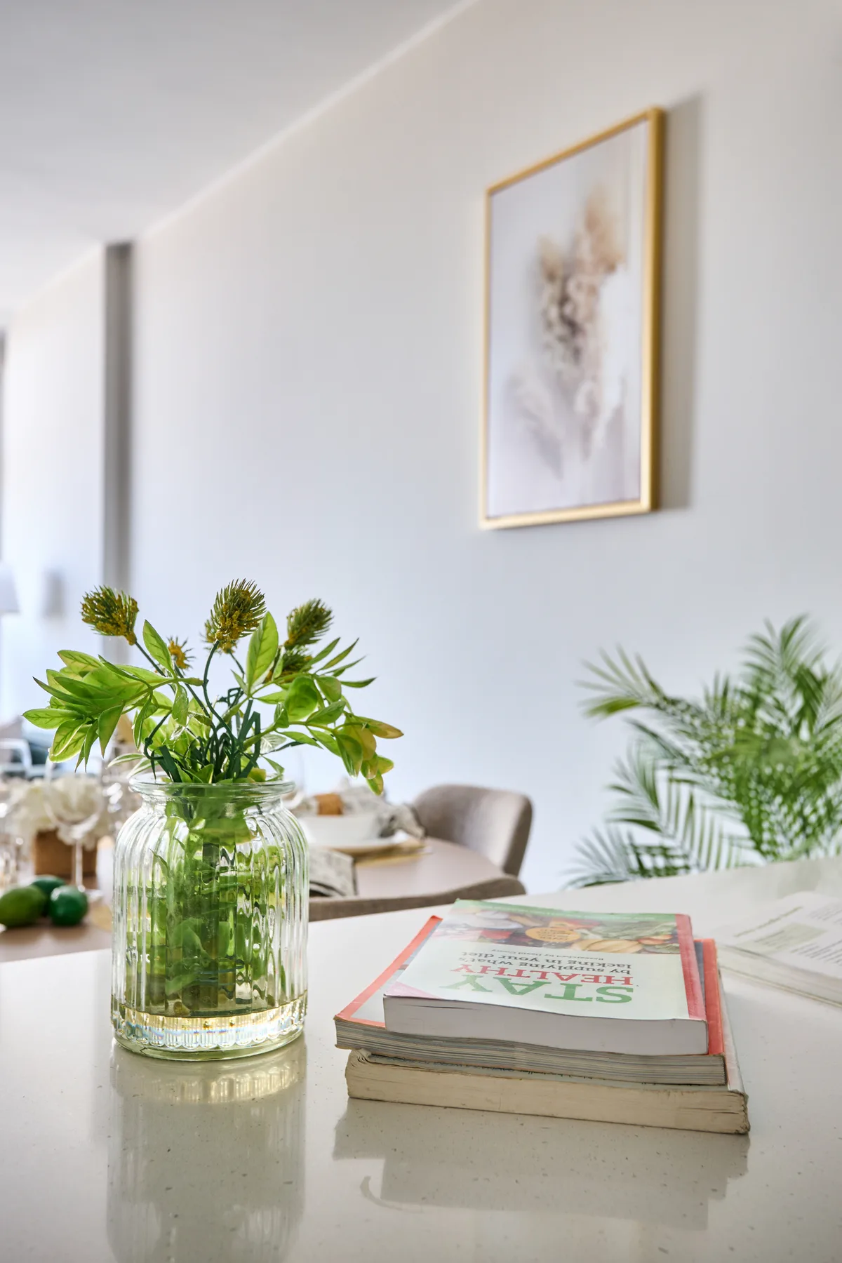 Una sala luminosa con un jarrón con plantas y libros sobre una mesa.