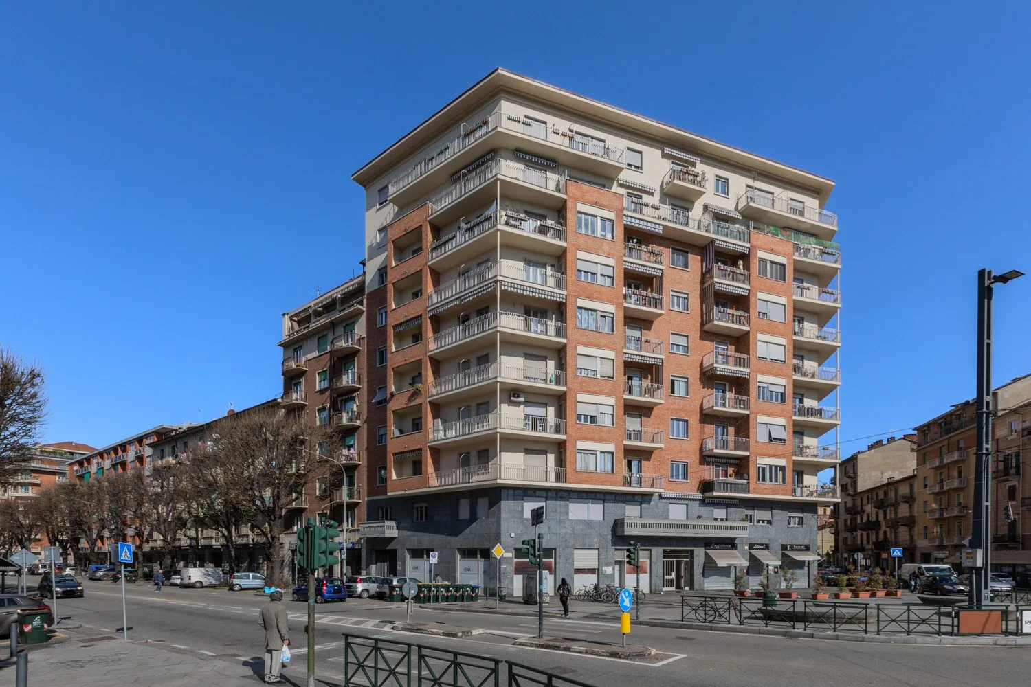 A multi-story apartment building stands along a city street beneath a clear blue sky.