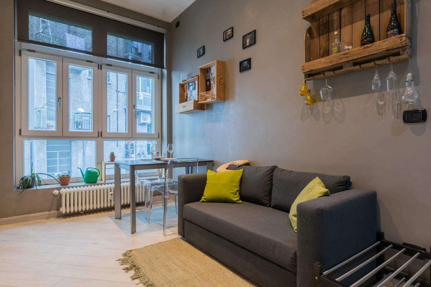 A living room with a dark sofa beside large windows and a small dining table.