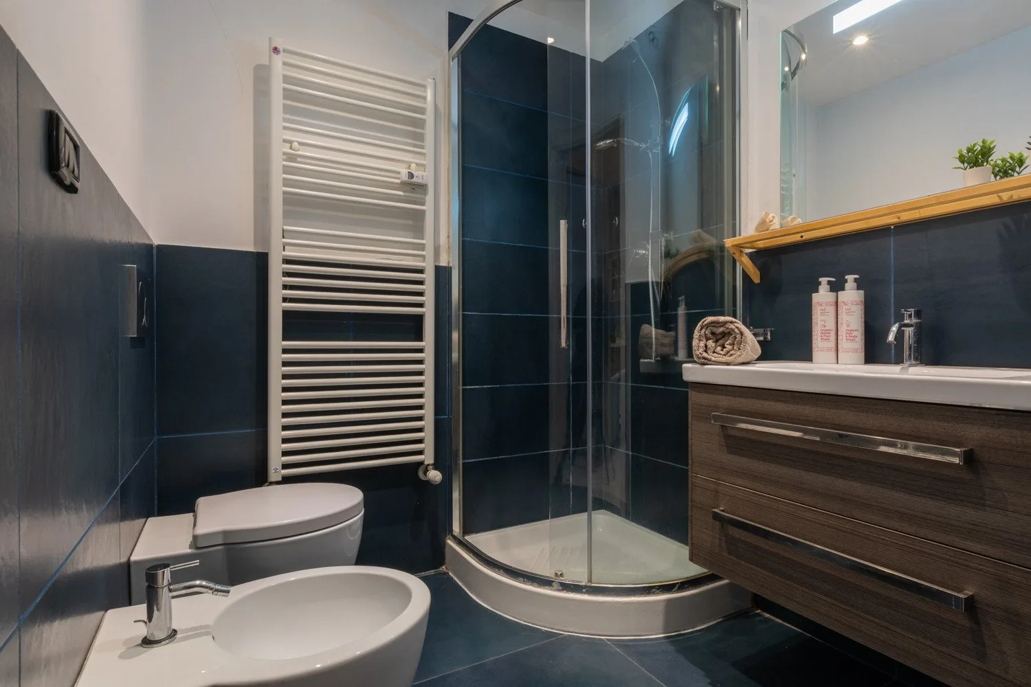A modern bathroom with a glass shower, sink, and dark tiled walls.