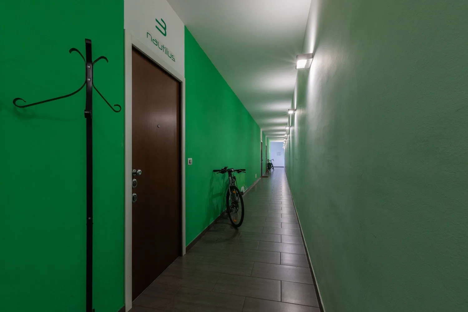 A long indoor hallway with green walls, doors, and a bicycle.