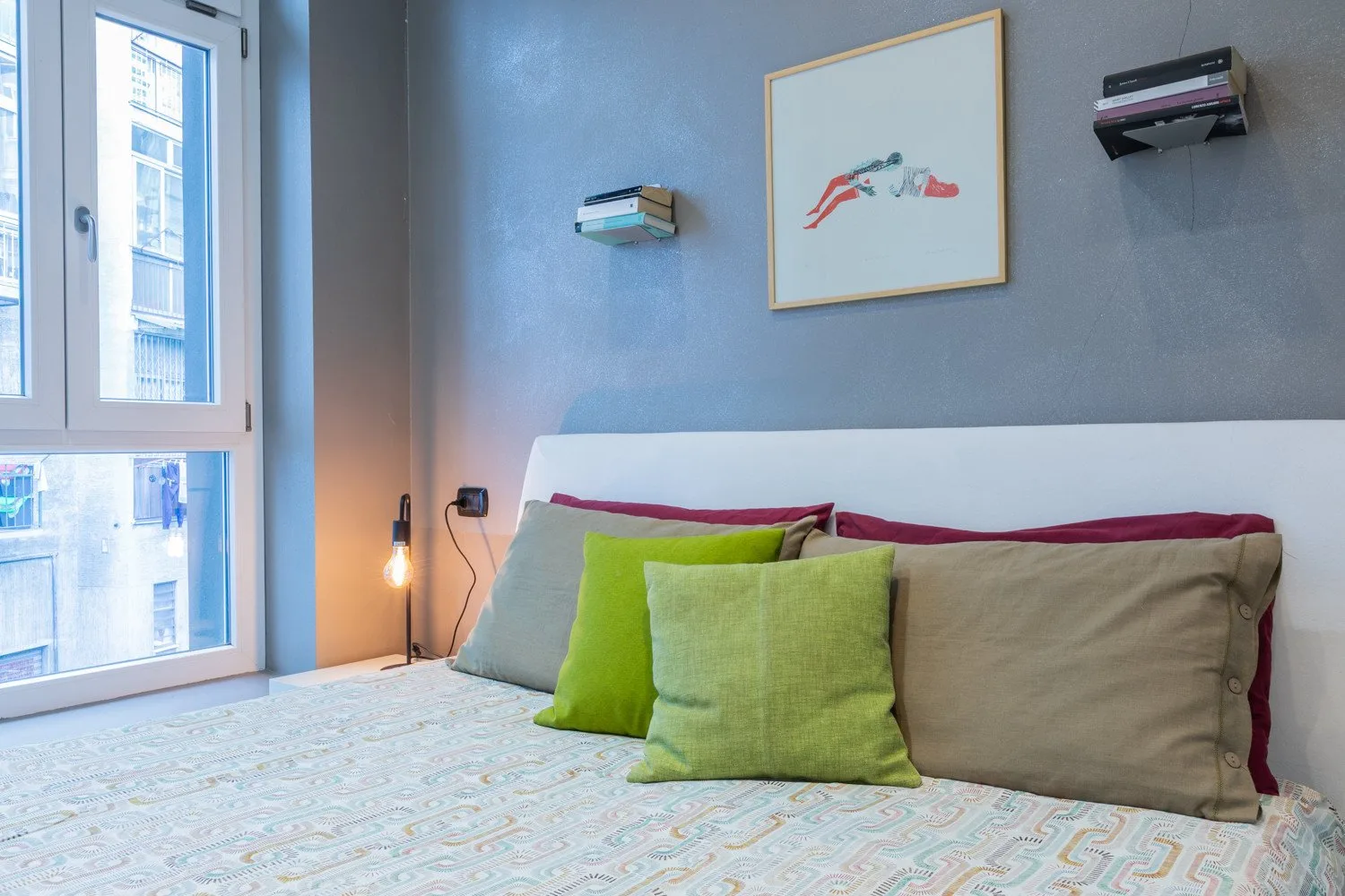 A bedroom with a bed, colorful pillows, and a large window.