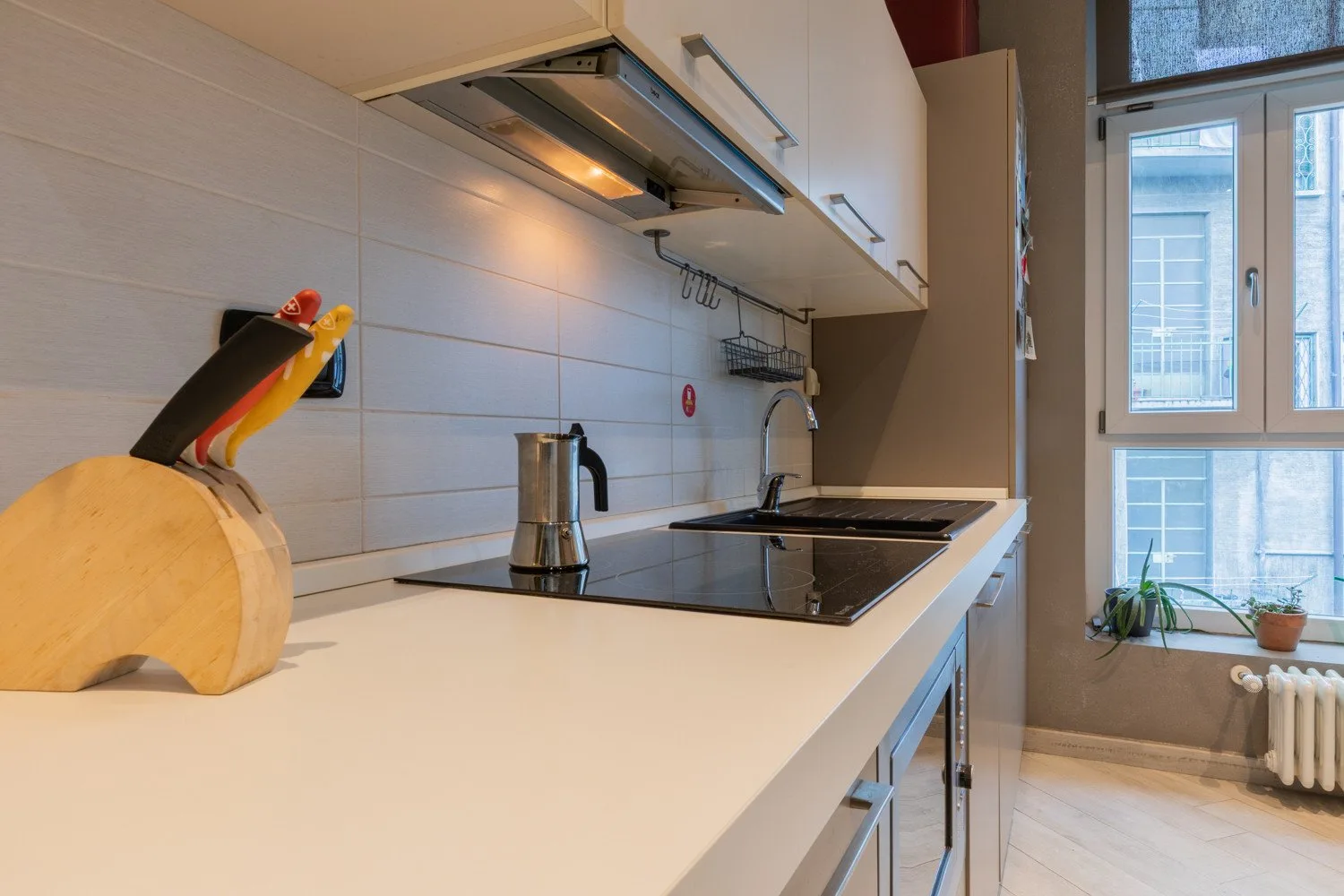 A bright kitchen with a long countertop, stovetop, and window.