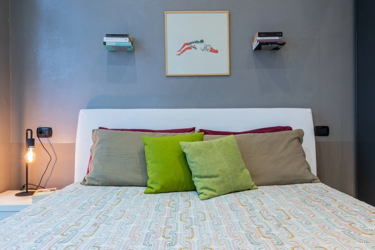 A bedroom with a neatly made bed and colorful pillows beneath framed artwork.