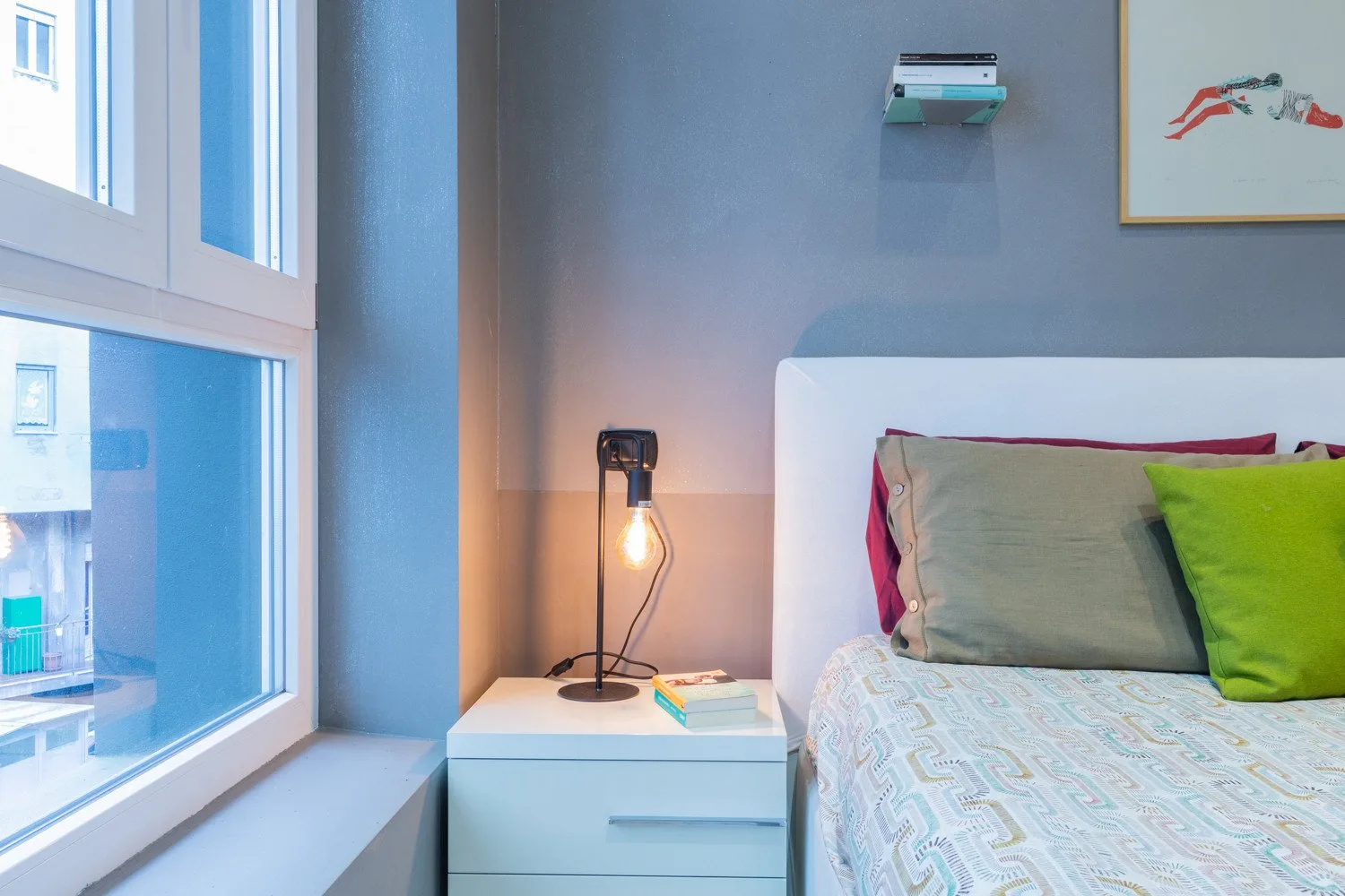 A bedroom with a bed beside a large window and a bedside table.