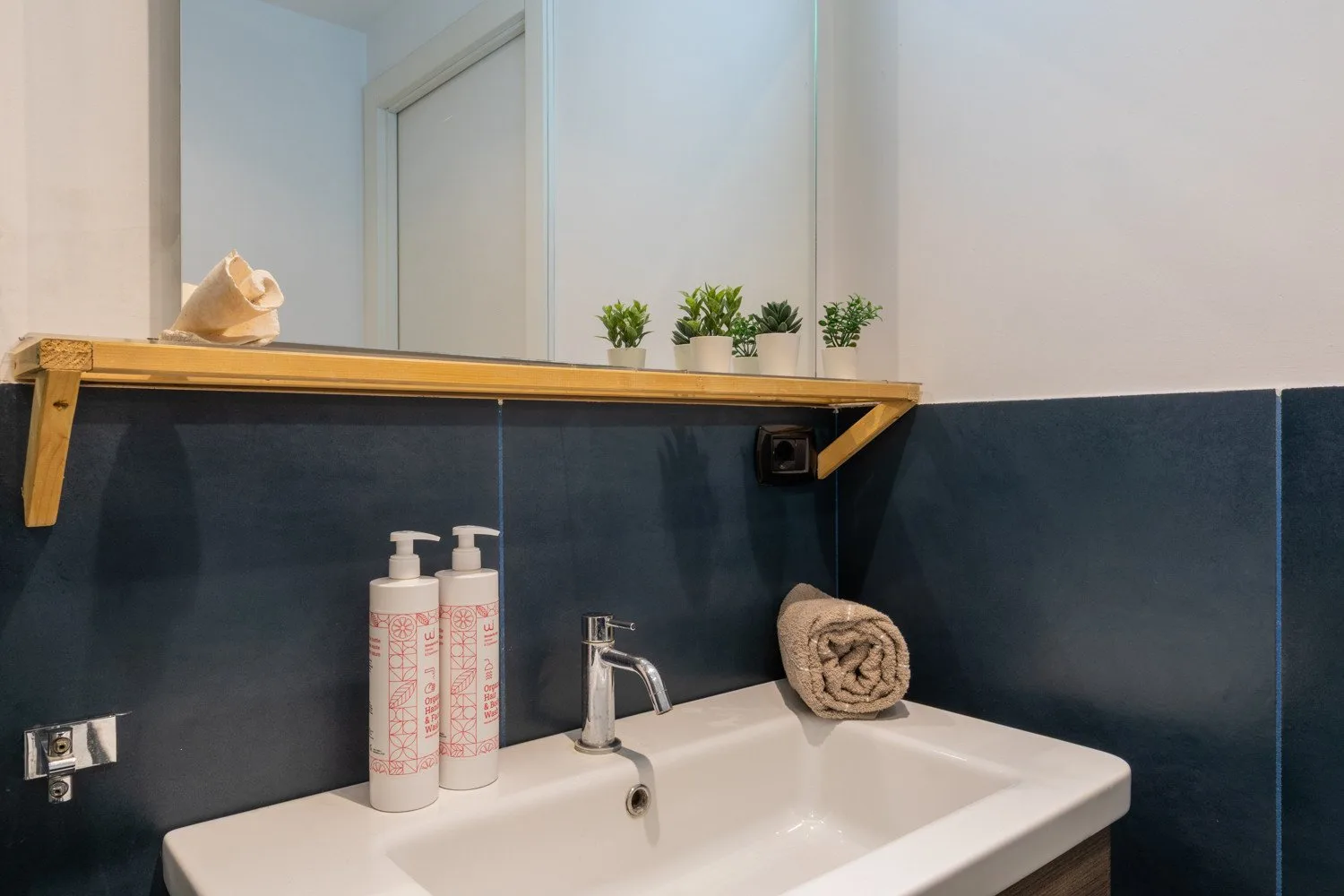 A bathroom sink with a faucet sits beneath a narrow shelf.