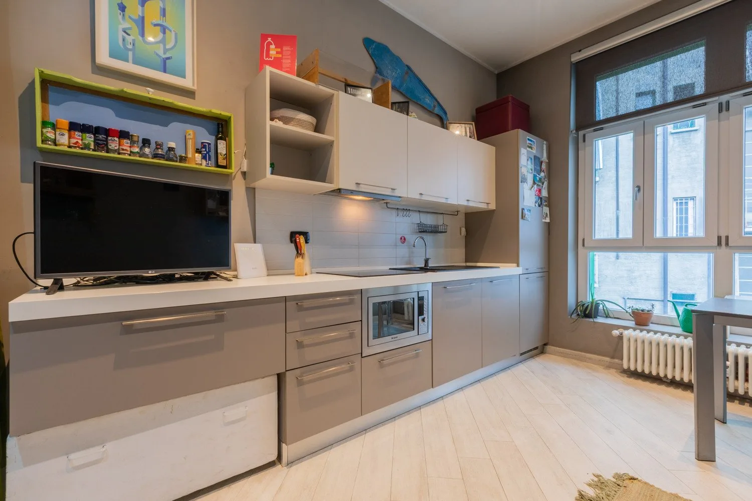 A compact kitchen with built-in cabinets, a countertop television, and large windows.