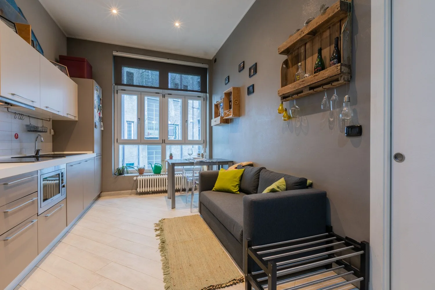 A narrow living and kitchen area with a gray seating area beside the dining table.