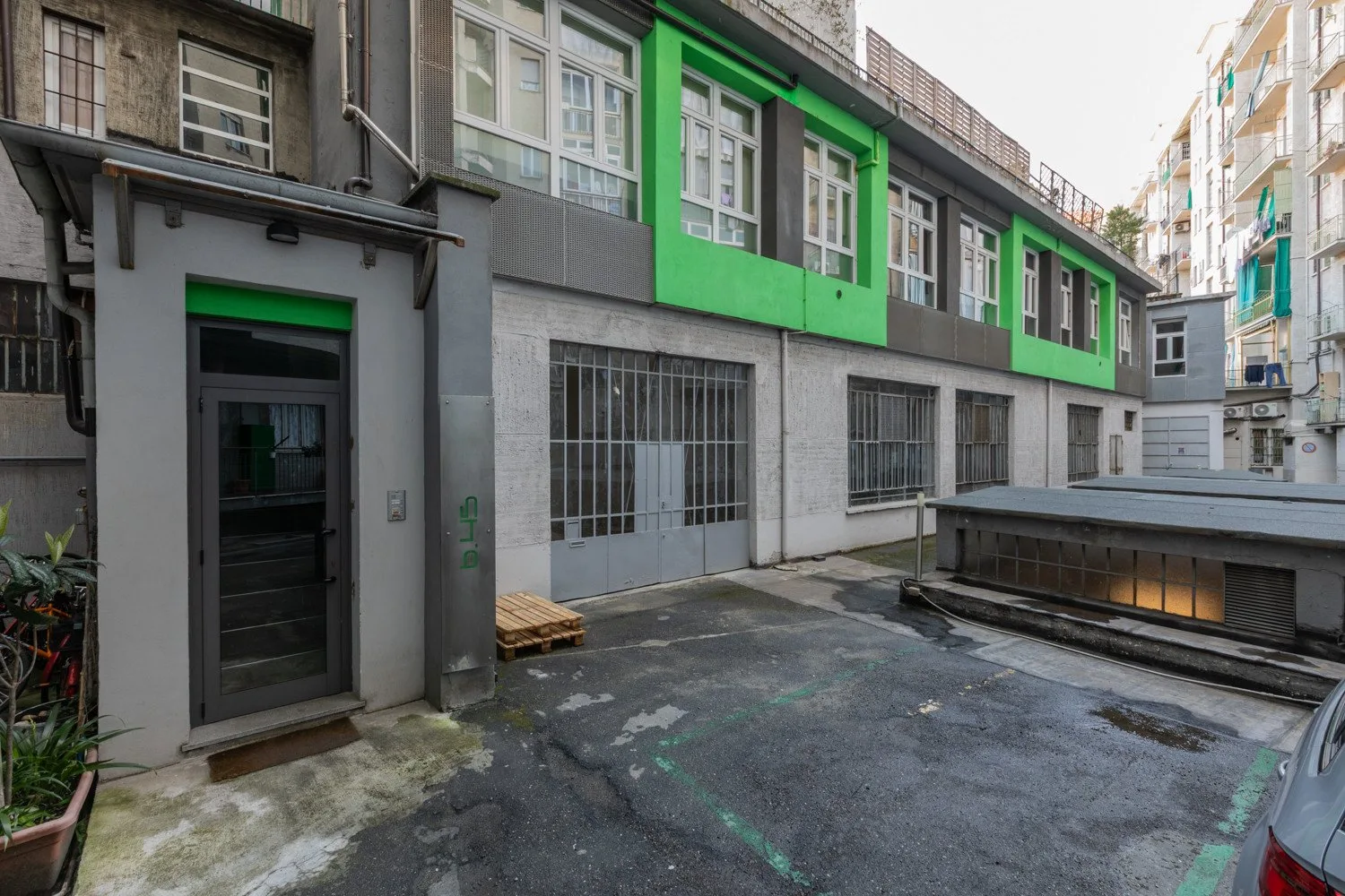 An urban courtyard beside a gray building with bright green window frames.