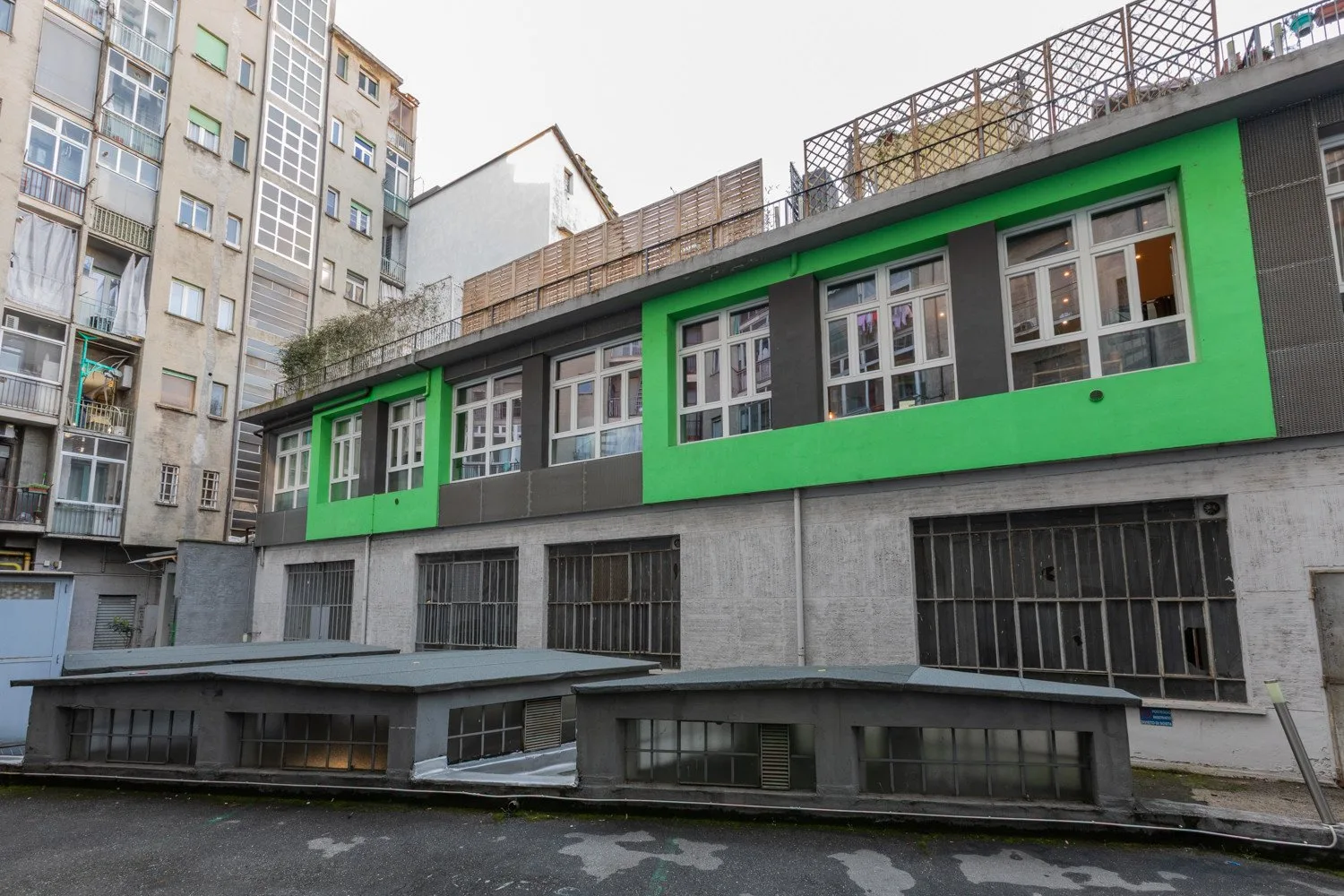 An urban building facade with bright green panels surrounding rows of windows.