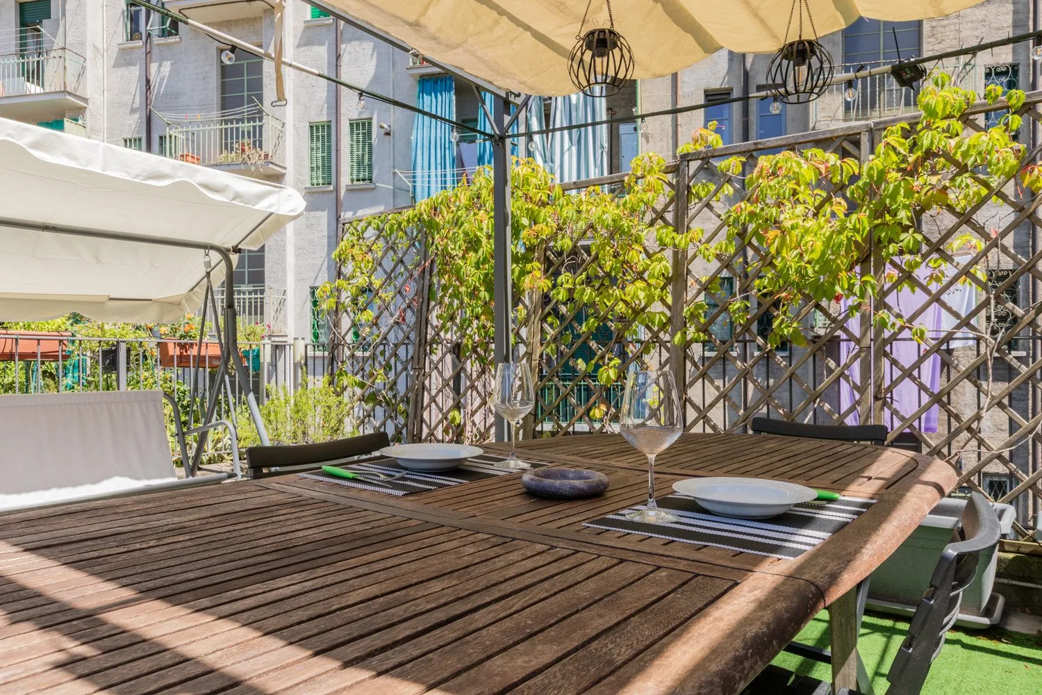 An outdoor dining terrace with a long wooden table and leafy trellis.