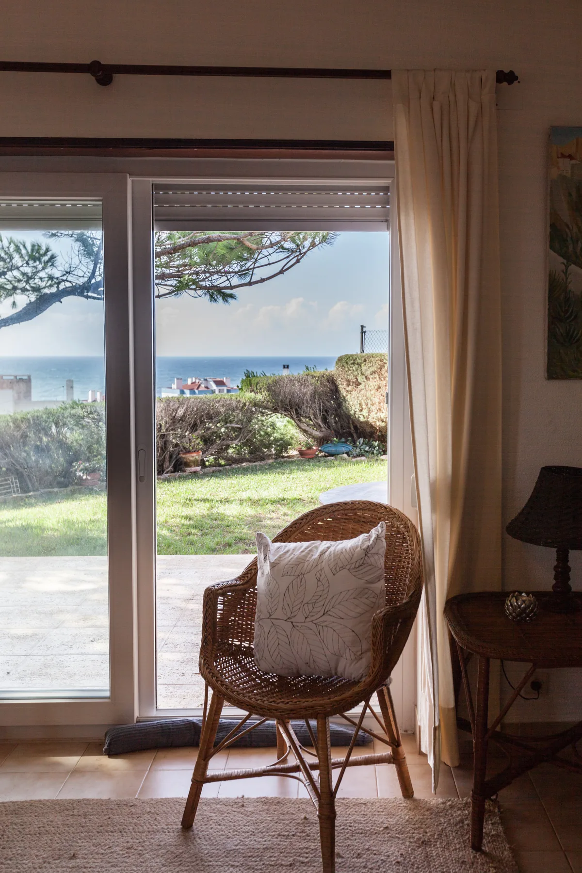 A sunlit seating area faces a garden and the ocean through glass doors.