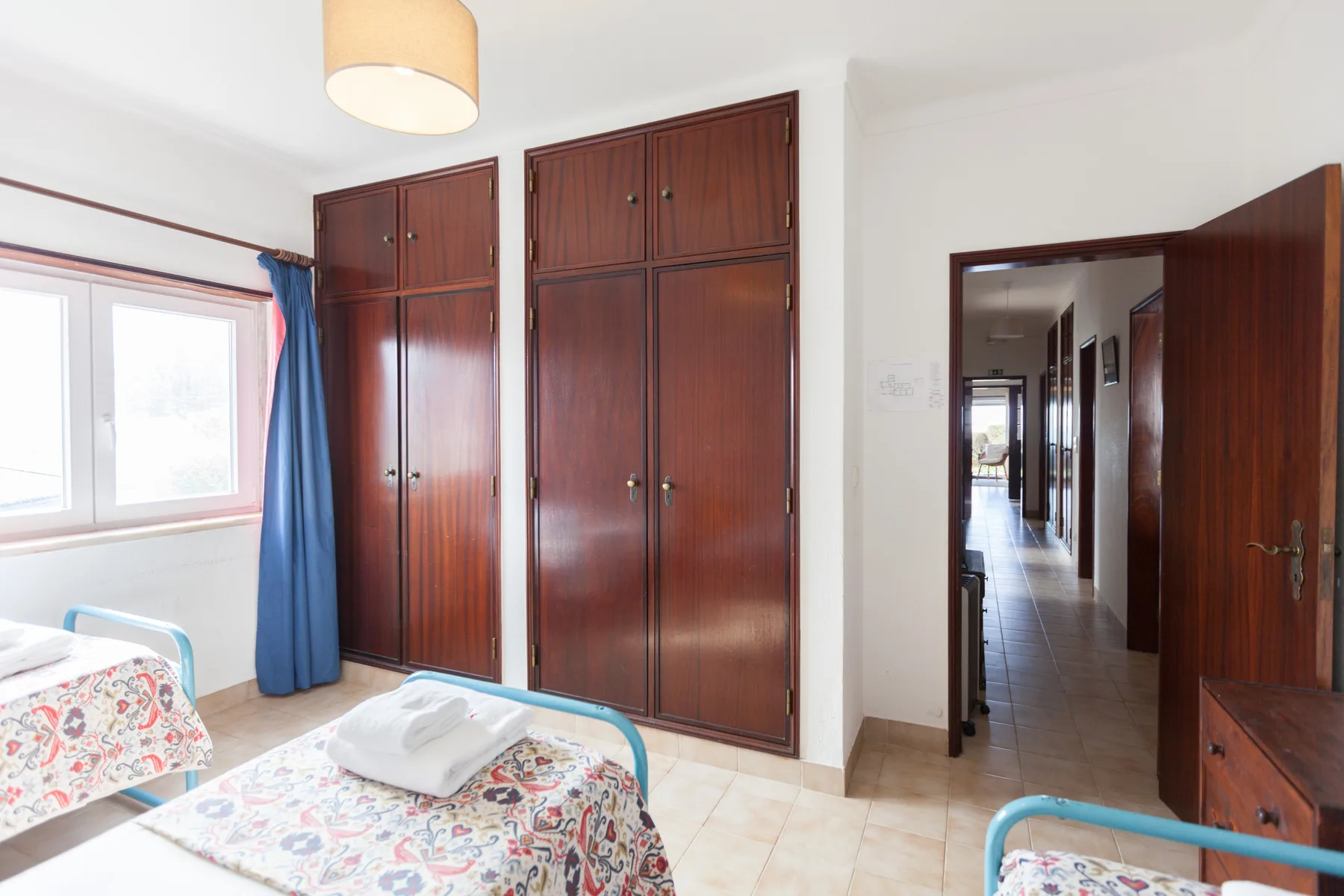 A bedroom with beds, tall wooden wardrobes, and an open doorway.