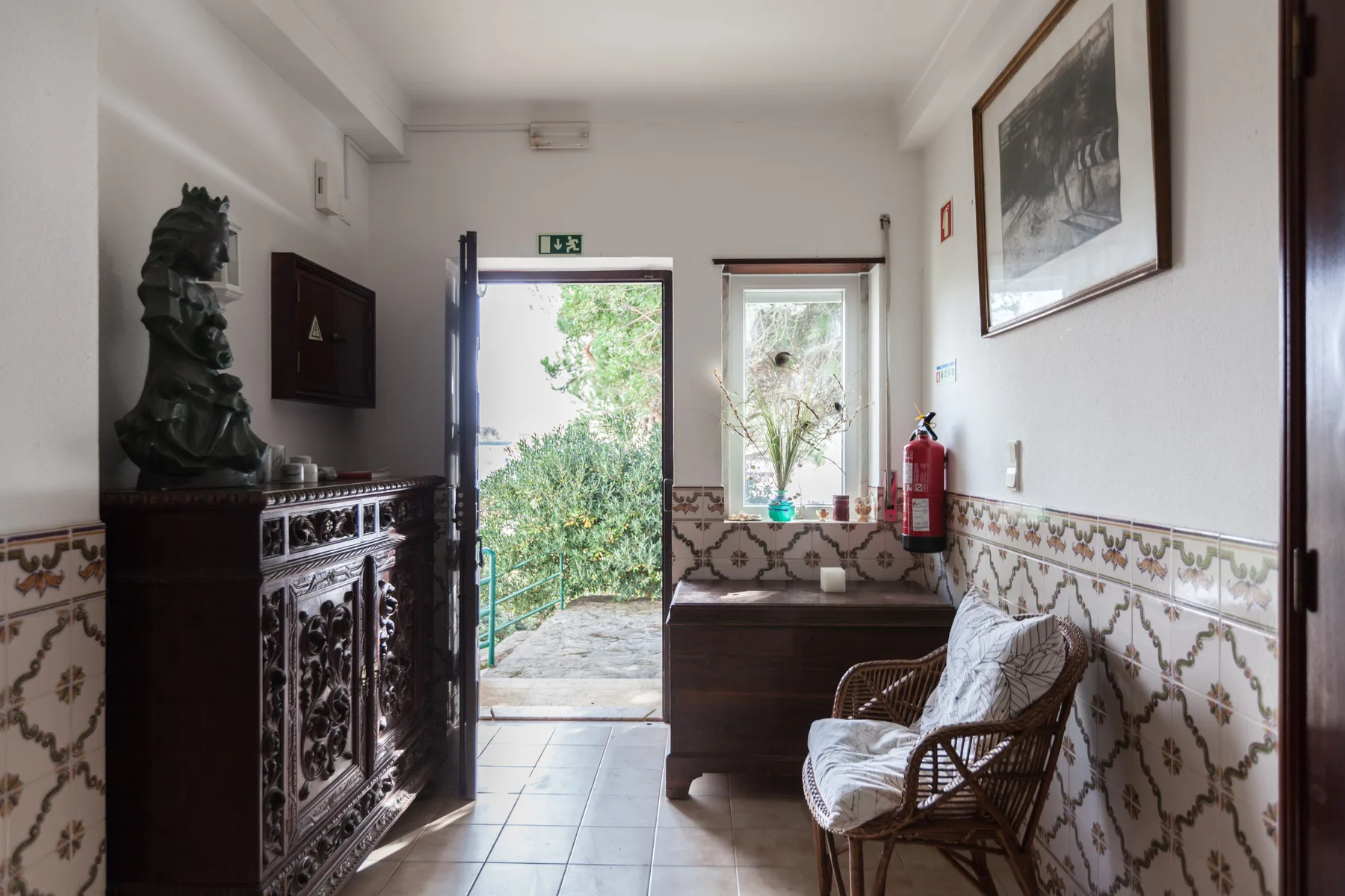 An entry hall with a dark cabinet, patterned tile, and a chair beside the open doorway.