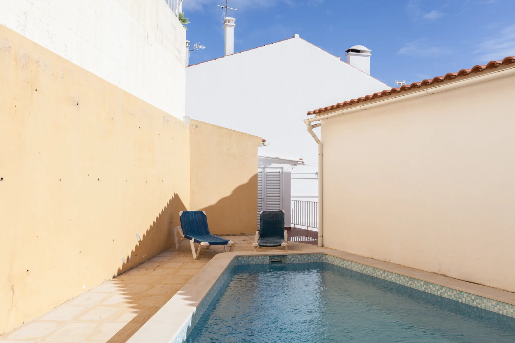 A small outdoor pool sits beside two lounge chairs in a sunny courtyard.