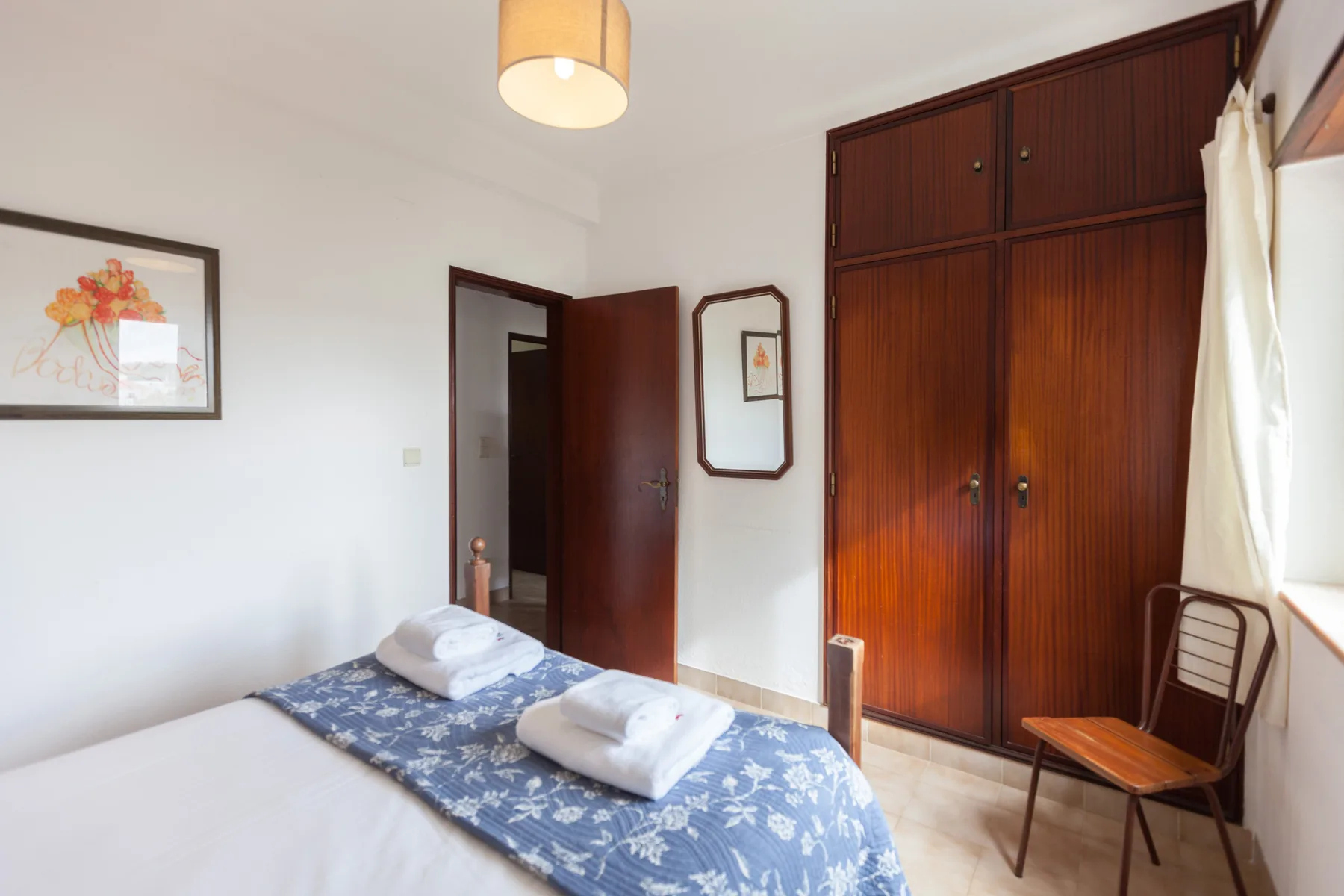 A bedroom with a bed, folded towels, and a large wooden wardrobe.