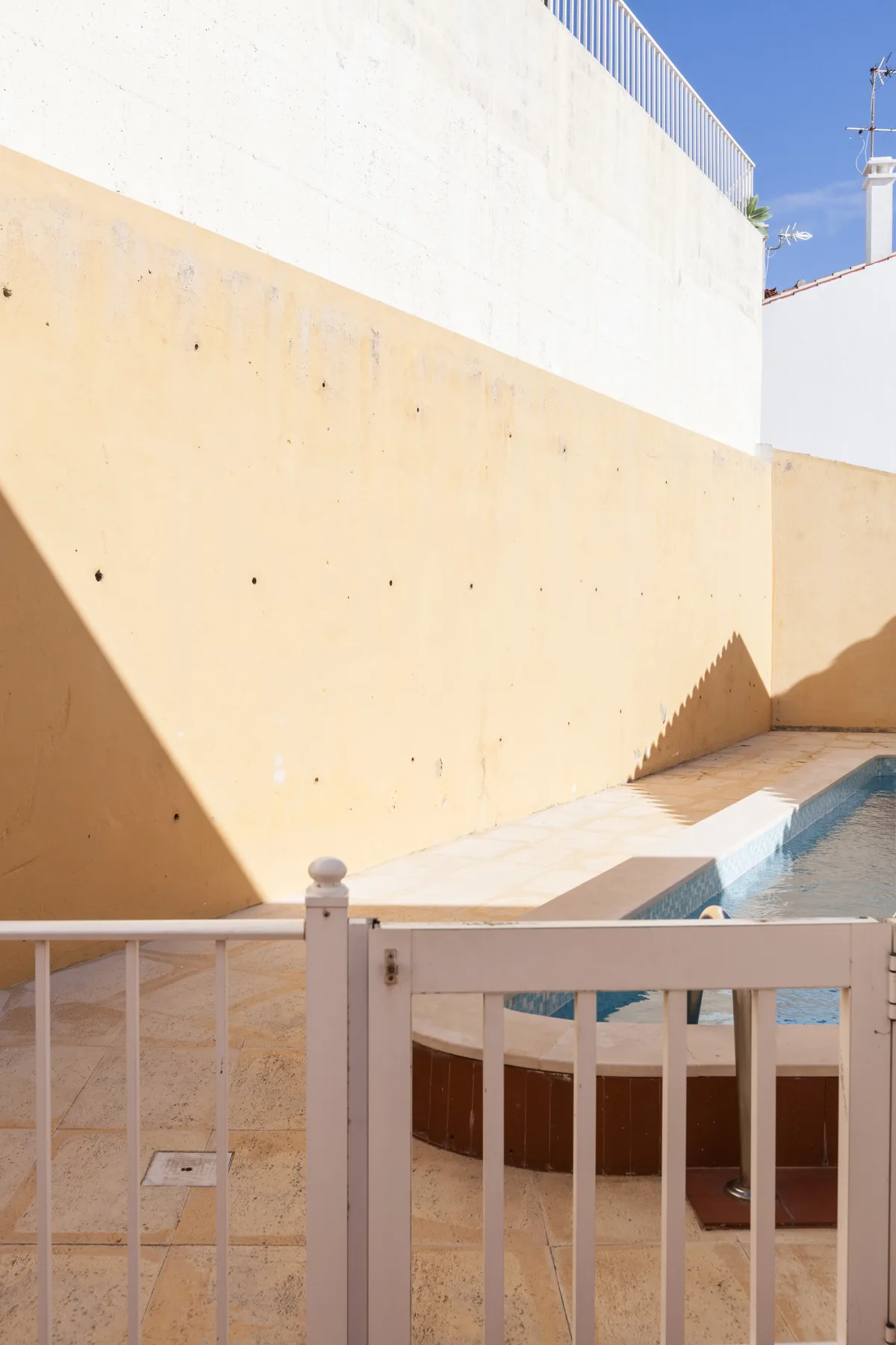 A small outdoor pool sits beside a sunlit courtyard wall.