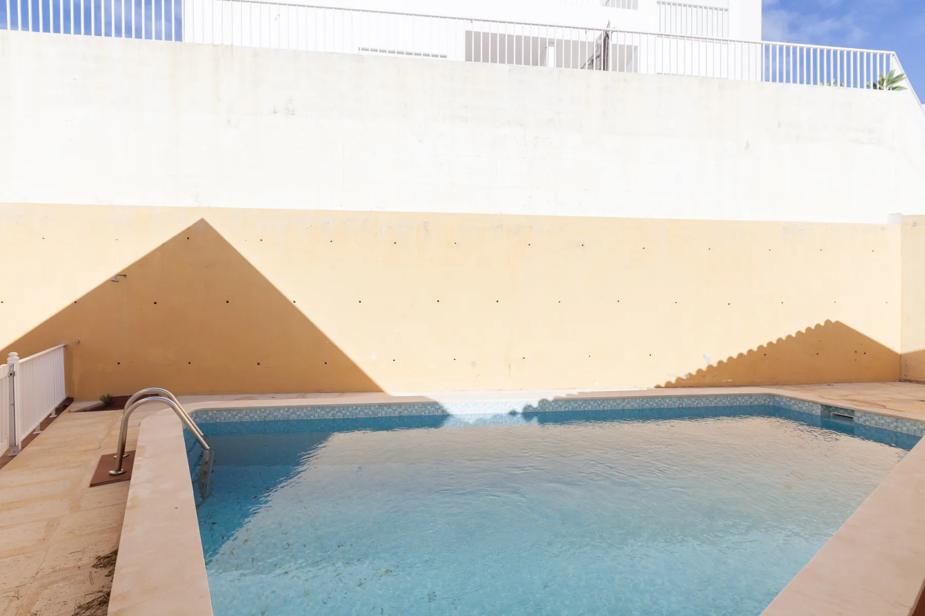 An outdoor swimming pool sits beside a pale wall.