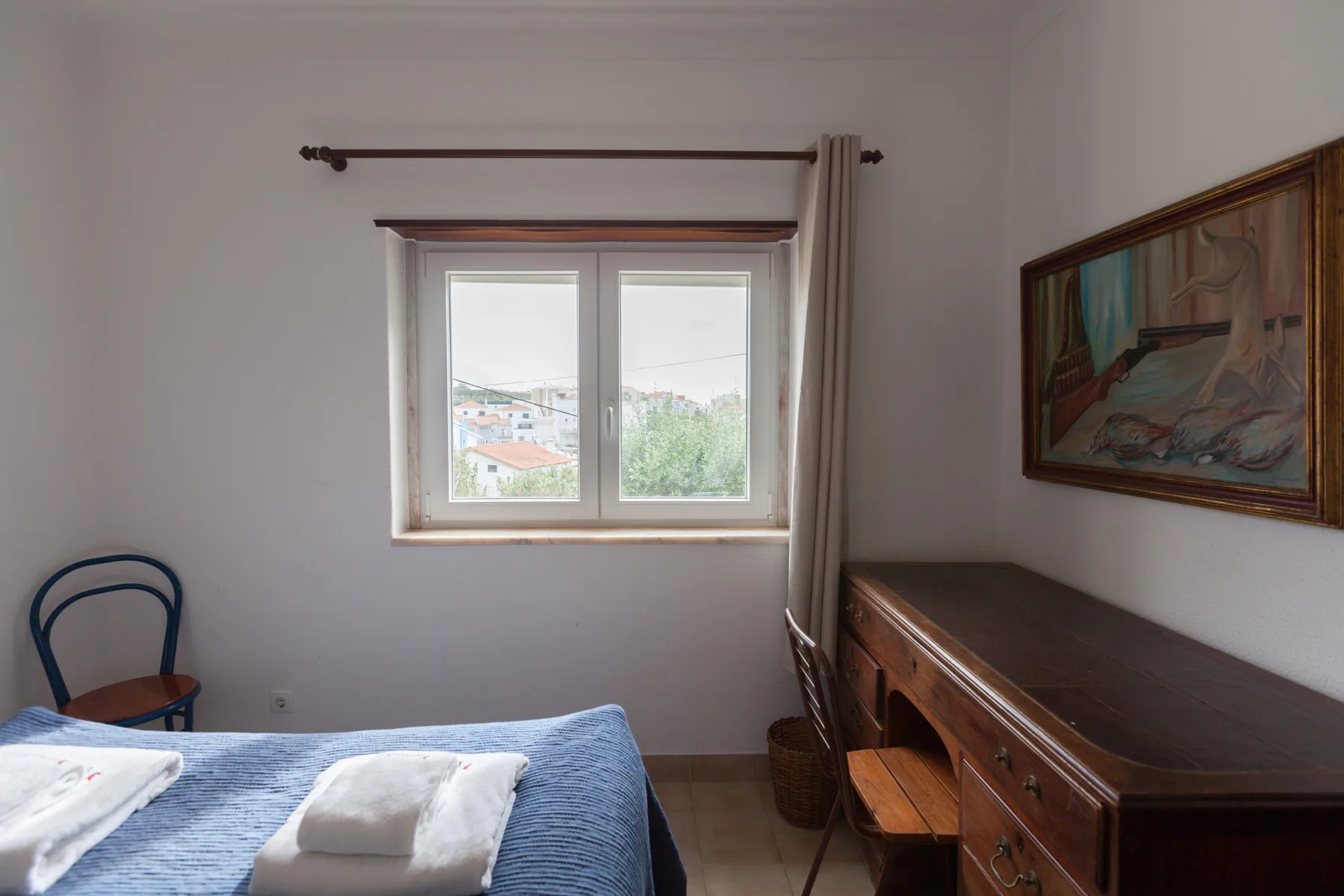 A bedroom with a blue-covered bed, a window, and wooden furniture.