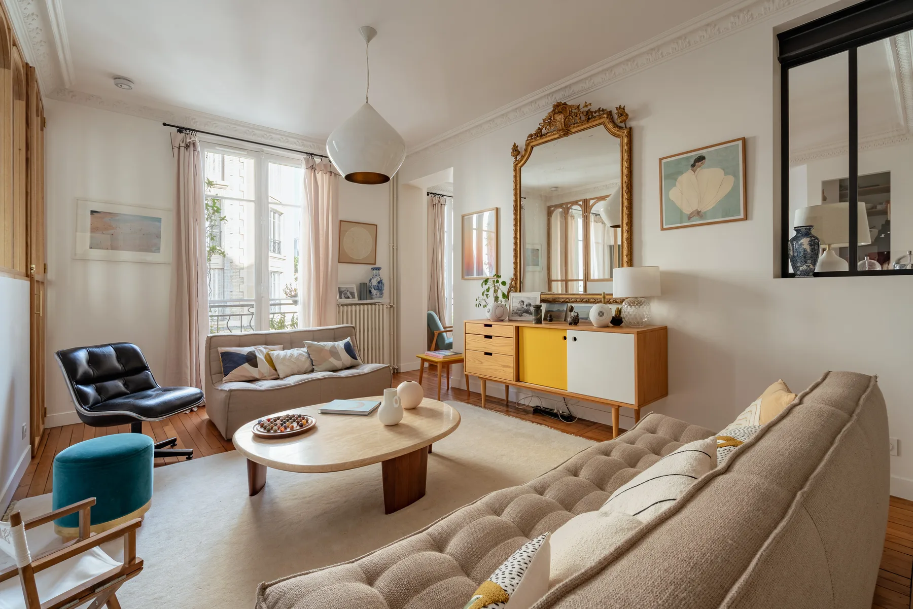 A bright living room with seating around a round coffee table and a wooden sideboard.